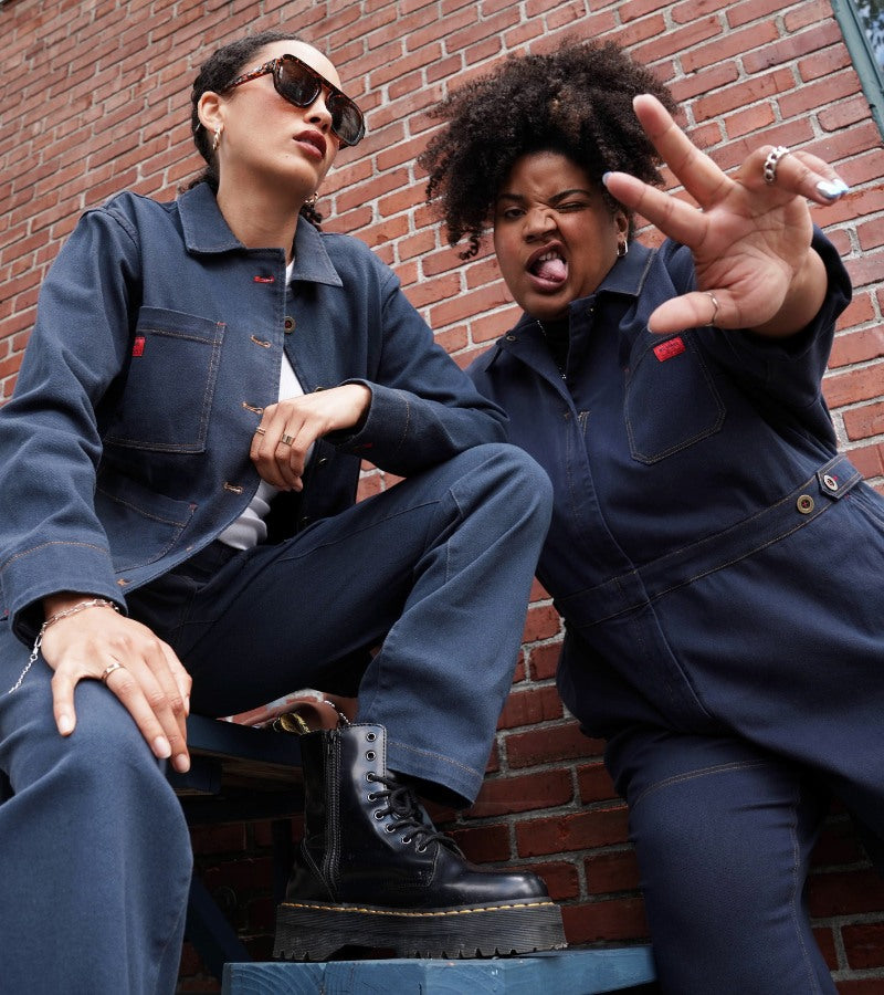 Two people standing in front of brick wall wearing navy denim pieces
