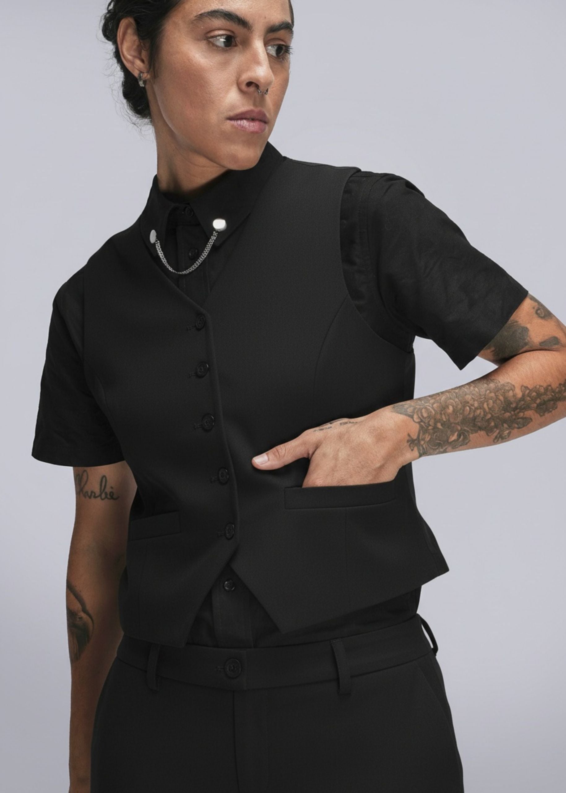 Person wearing a black outfit with chain collar clips on a plain background
