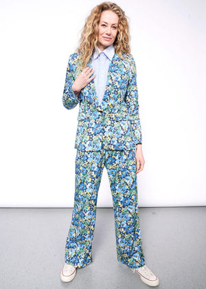 S=Person with wavy blonde hair looks at camera wearing light blue button up and floral patterned suit.