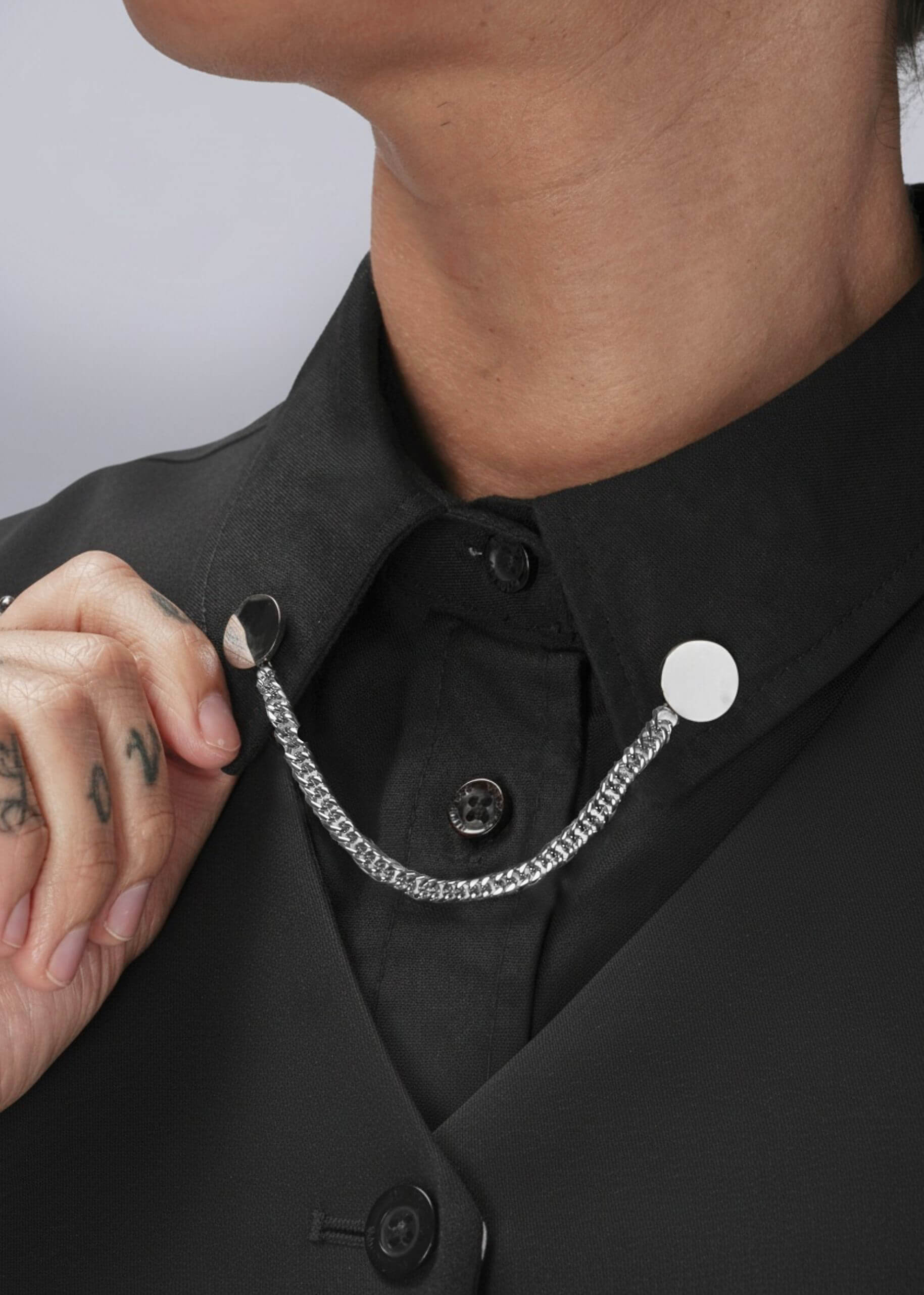 Person wearing a black shirt with silver chain collar clips on a plain background