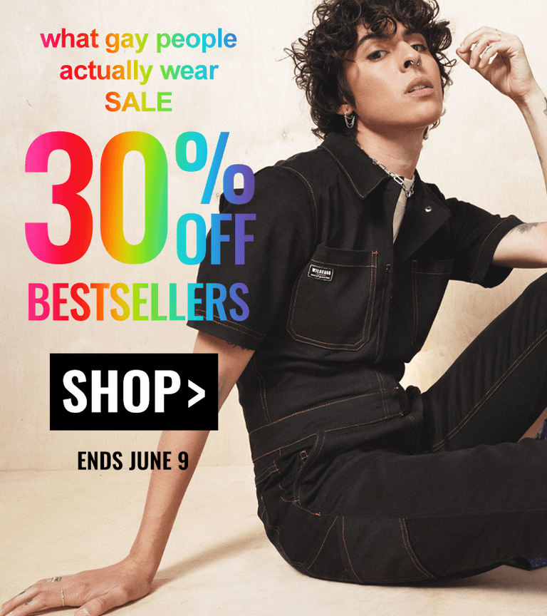 Against wood background, model sits on ground wearing The Essential Coverall in black. Overlay text reads "what gay people actually wear sale 30% off bestsellers. shop. ends june 9"