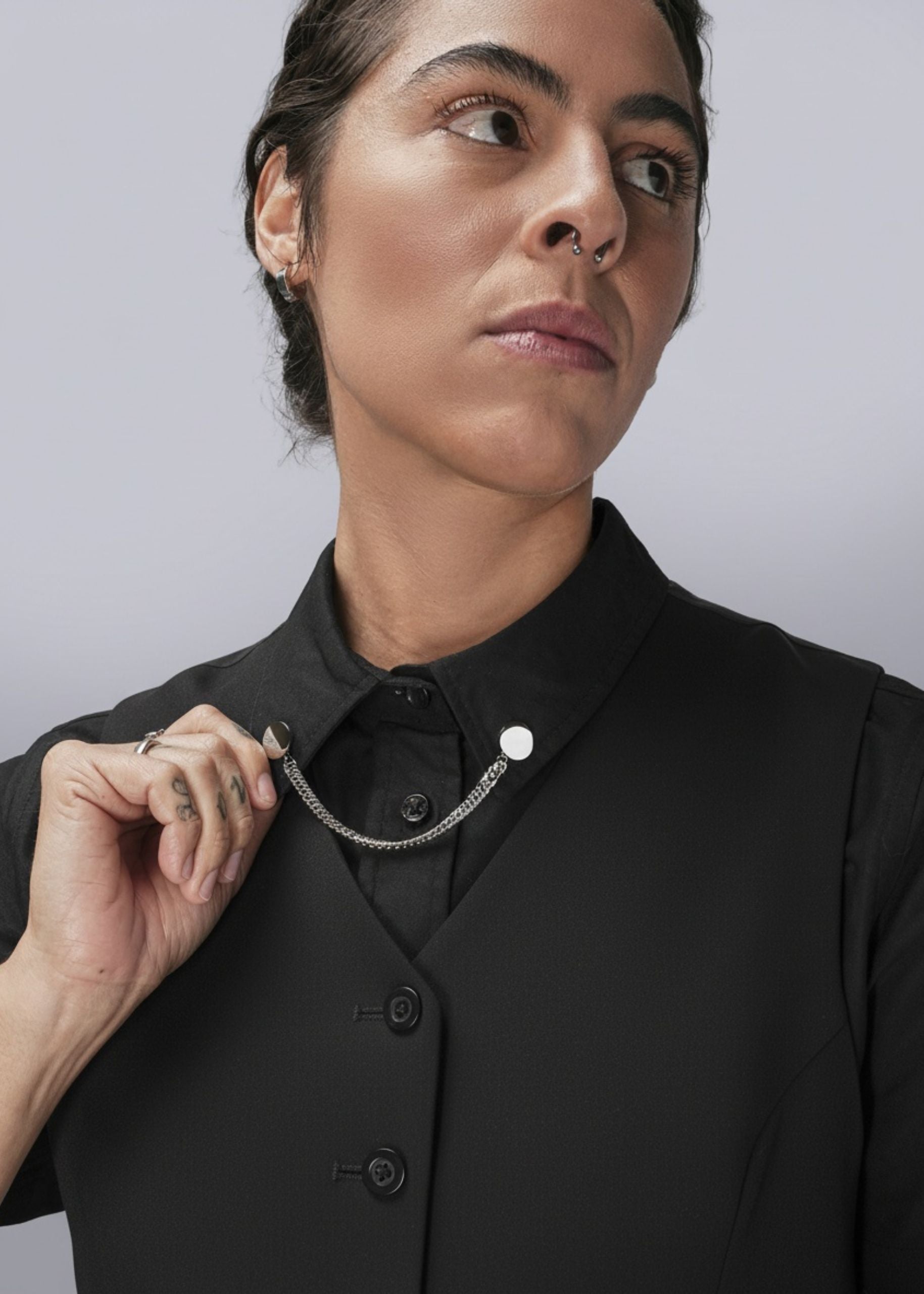 Person wearing a black shirt with a chain collar clips on a plain background