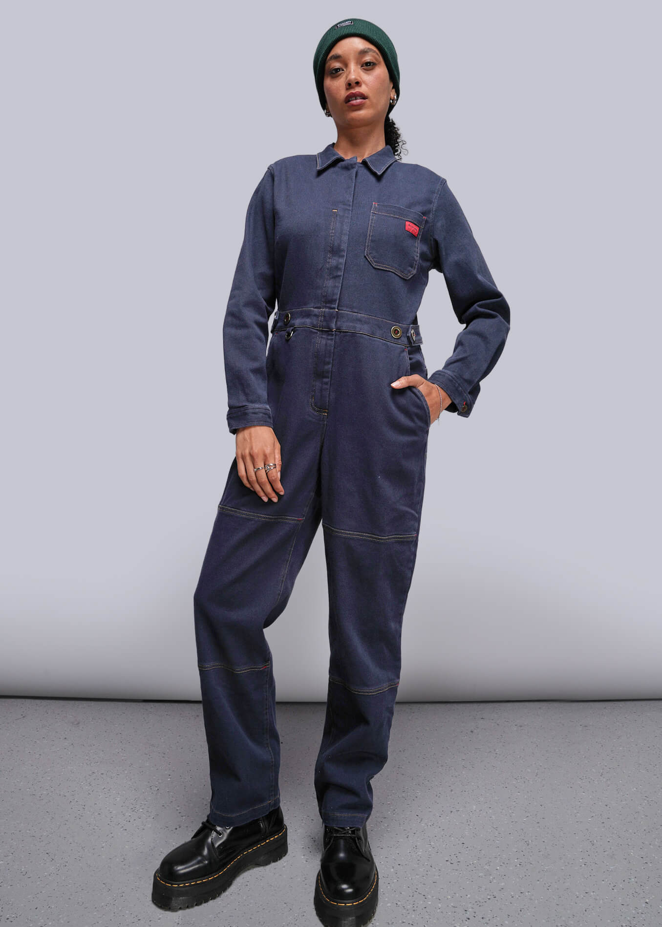 Person wearing a navy blue jumpsuit with a red pocket patch on a plain background