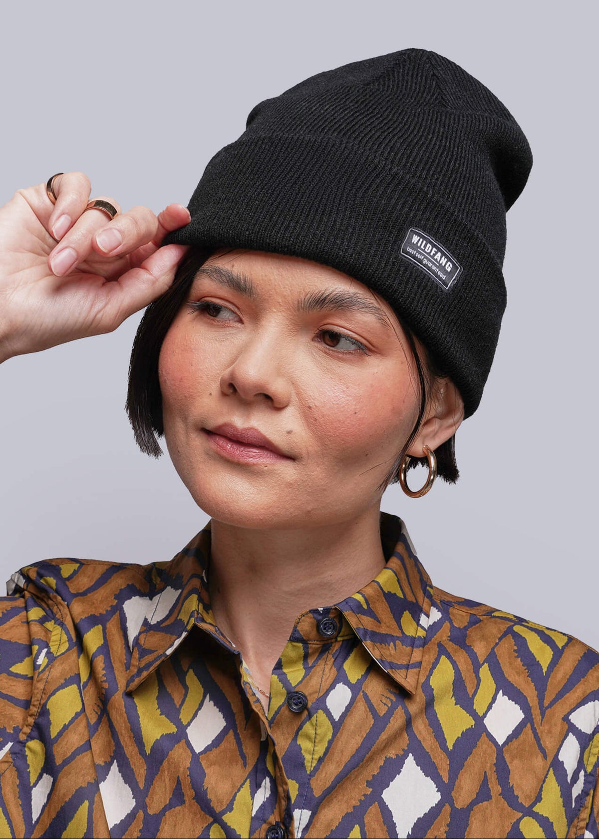 Person wearing a black beanie with brand label and a patterned button up shirt