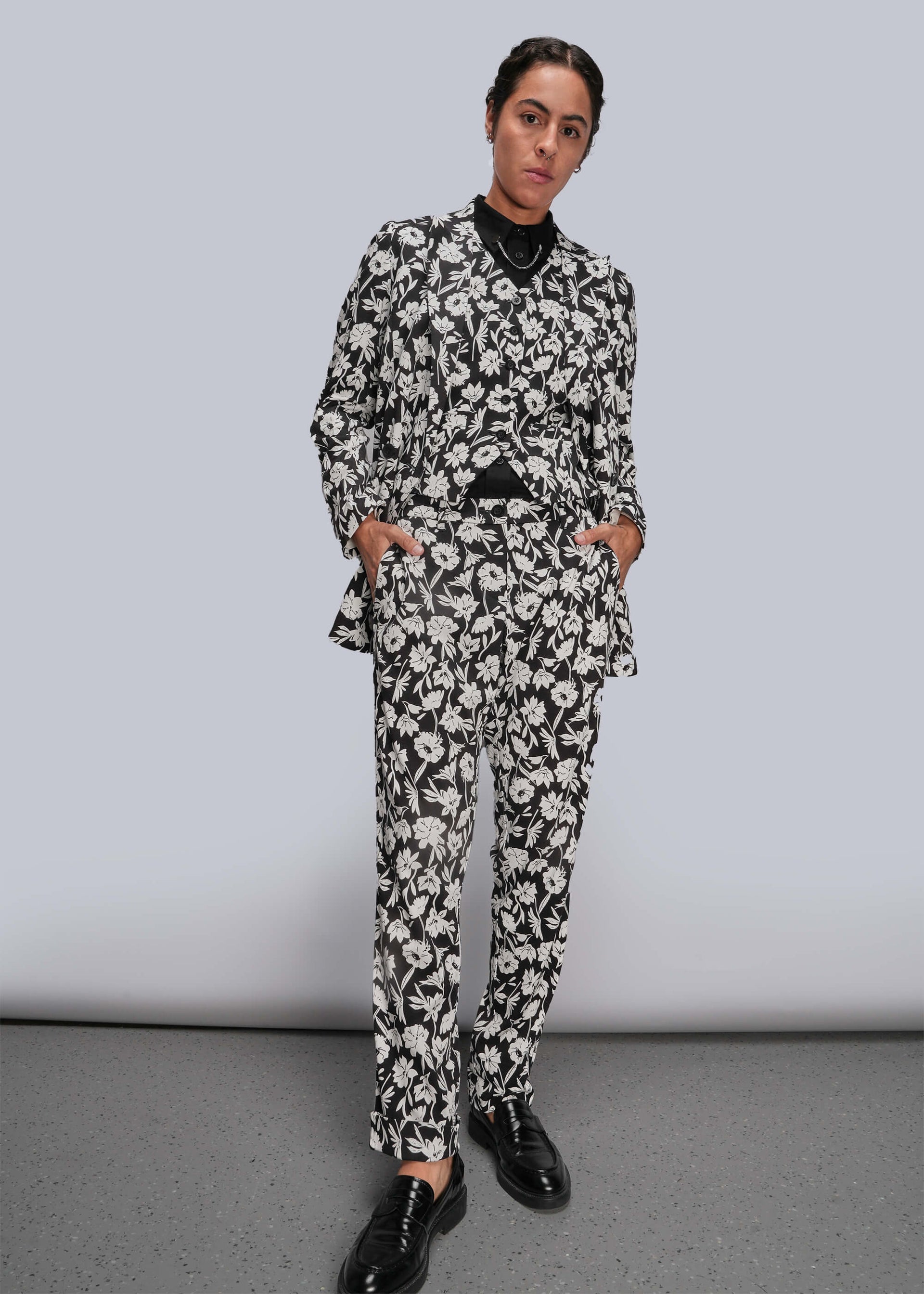 S=Person wearing a black and white floral suit against a plain background