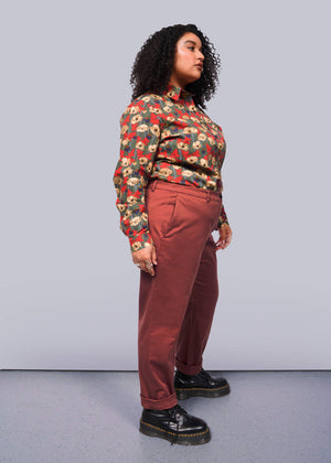 1X=With their curly hair, a person confidently wears The Essential Trouser featuring a relaxed mid-rise fit. A colorful floral blouse tops the wardrobe staple, paired with black platform shoes for an edgy touch. The plain white background highlights their stylish ensemble.