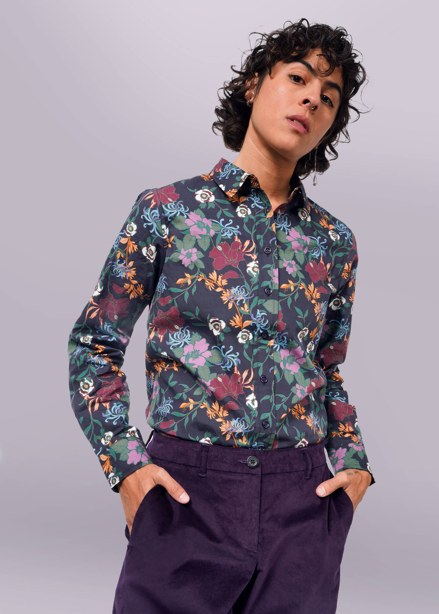 S= A person wearing a long sleeve button-up shirt with a floral pattern and button cuffs. The shirt is primarily navy with multicolored floral accents.
