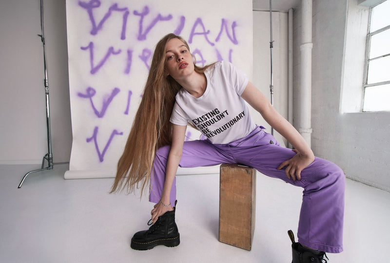 Vivian WIlson sits in front of backdrop while her name spray painted on it while wearing white shirt and purple coverall.