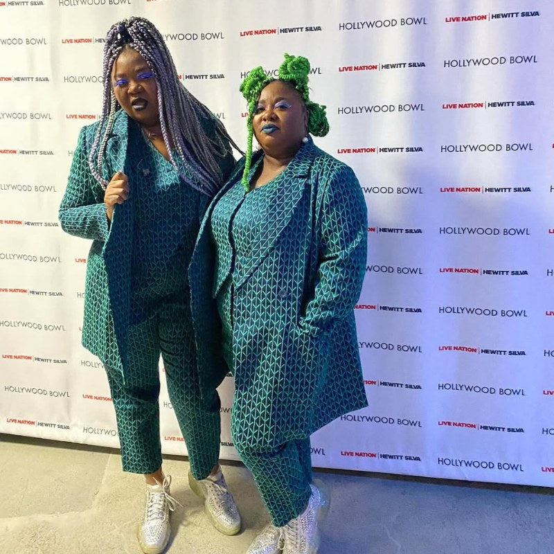 Two women wearing blue patterned suits, stand in front of backdrop with logos.