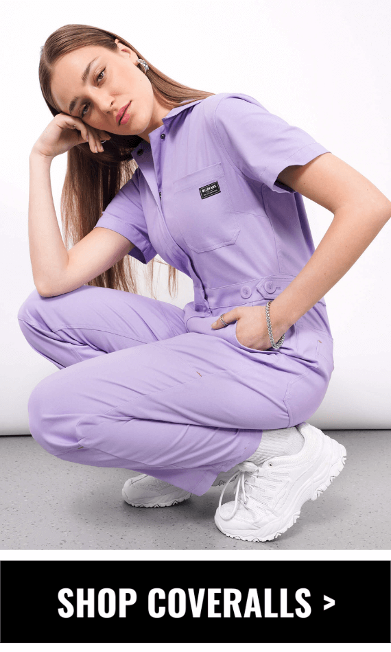 Model with long blonde hair wears The Essential High Waisted Coverall in Lilac. They are crouching down with one hand resting on their knee touching their face and the other in a side pocket. Underneath this image is a black button that says SHOP COVERALLS.