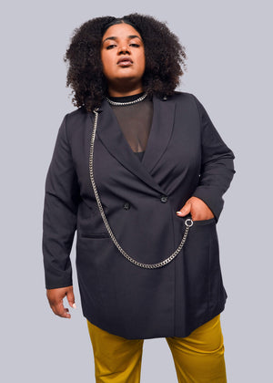 1X= A person with curly hair confidently poses in a stylish Debbie Harry X Wildfang Double Breasted Blazer, featuring intricate metal detailing over a sheer black top and vibrant yellow pants, set against a plain white background.
