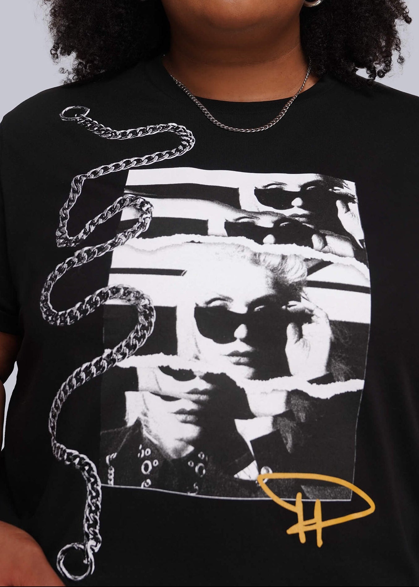1X=A plus-size model wearing a black graphic t-shirt with a white and black striped photo print, a silver chain design, and a yellow 'DH' logo on the front, set against a solid gray background.