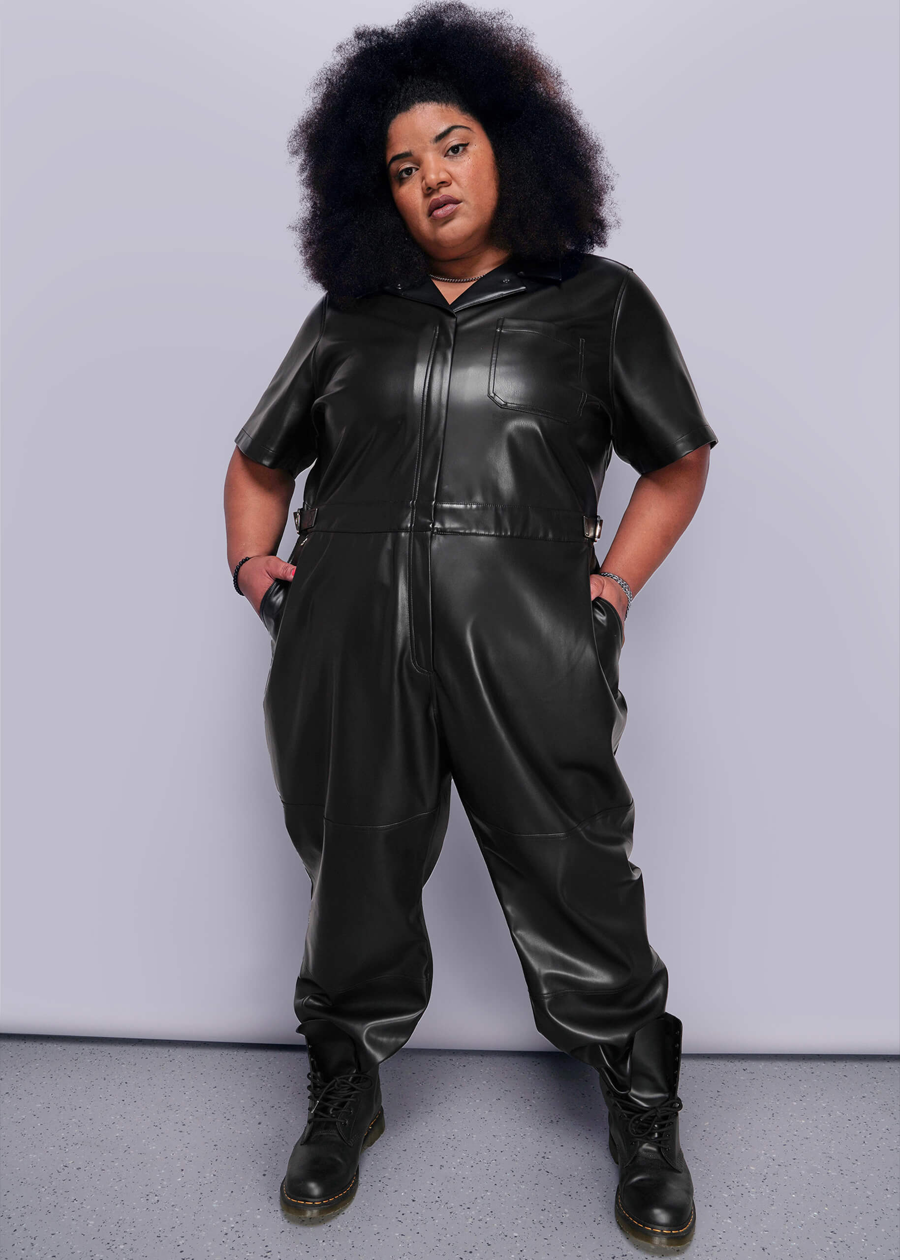 1X=Person wearing a black vegan leather jumpsuit against a plain background