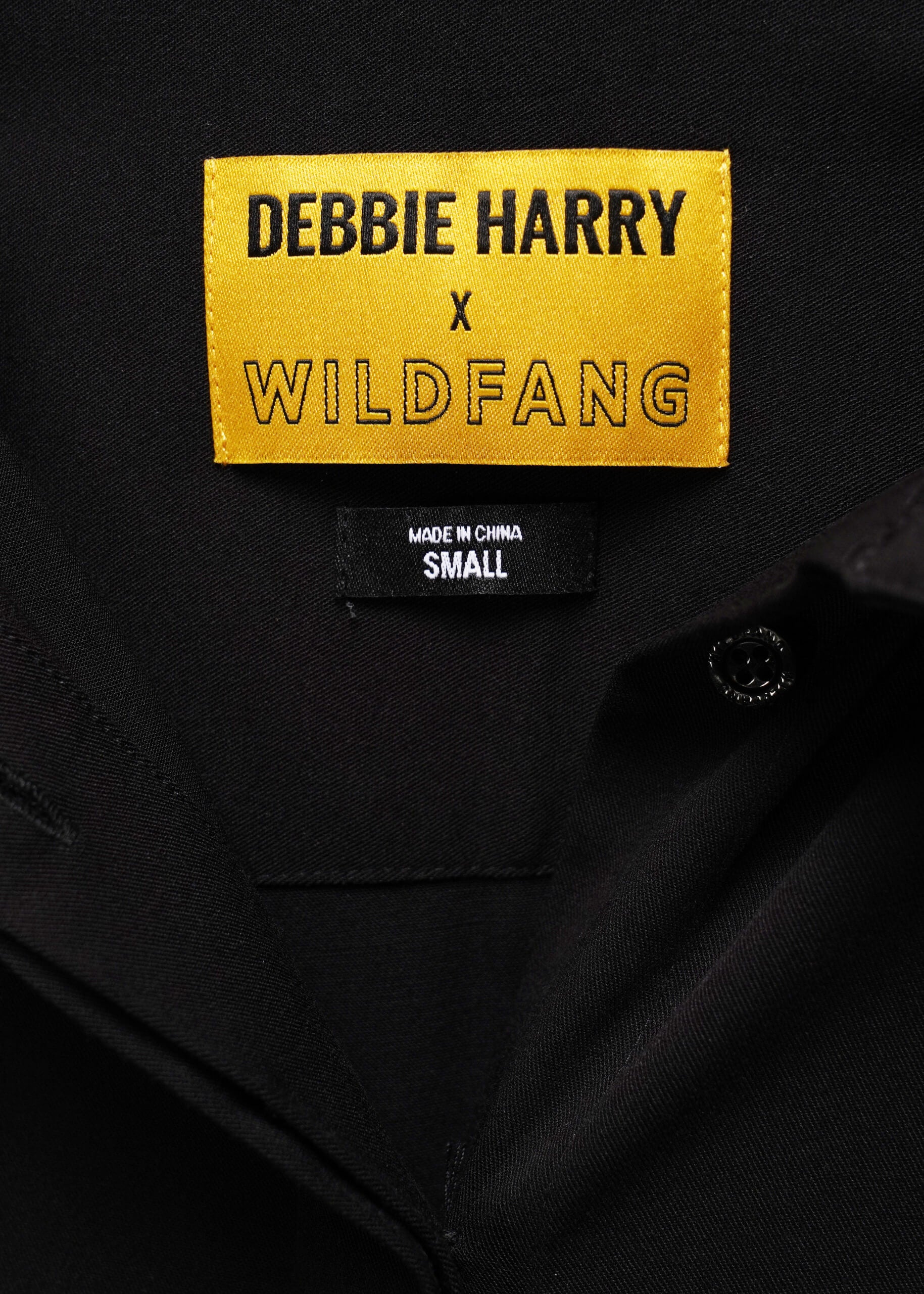 Close-up of a black Debbie Harry x Wildfang garment showing a bright yellow brand label and a black size tag reading SMALL.