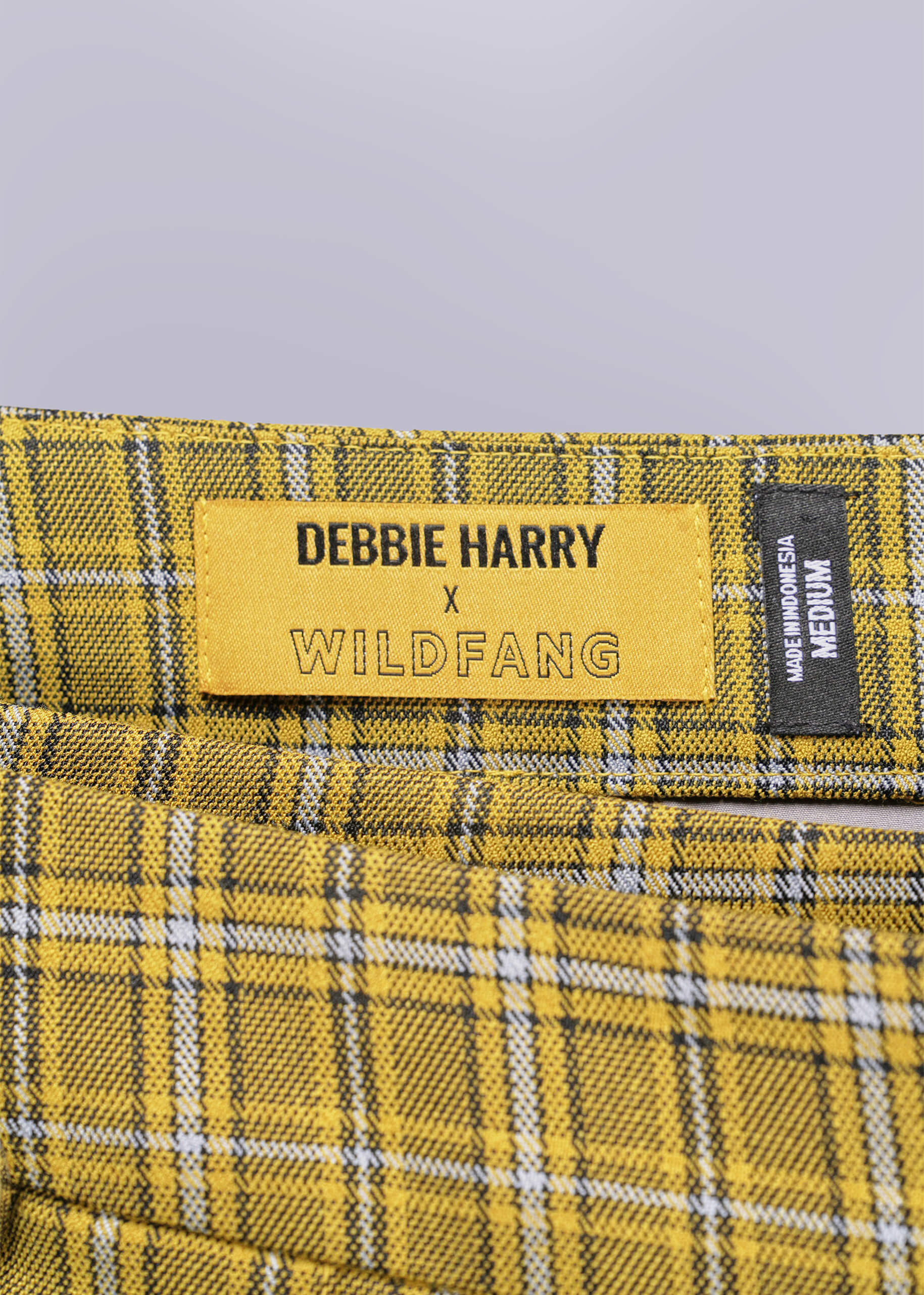 Close-up of a yellow label on plaid fabric with 'Debbie Harry x Wildfang' text.