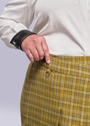 1X=Close up of person wearing a white shirt and yellow plaid skirt with a plain background