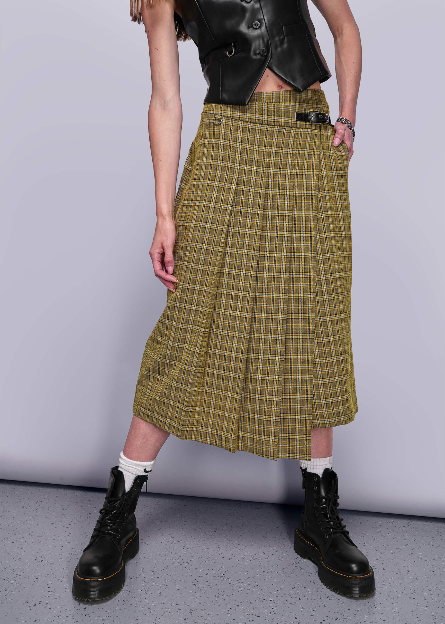 S=From chest down person wearing a yellow plaid skirt with black boots on a plain background