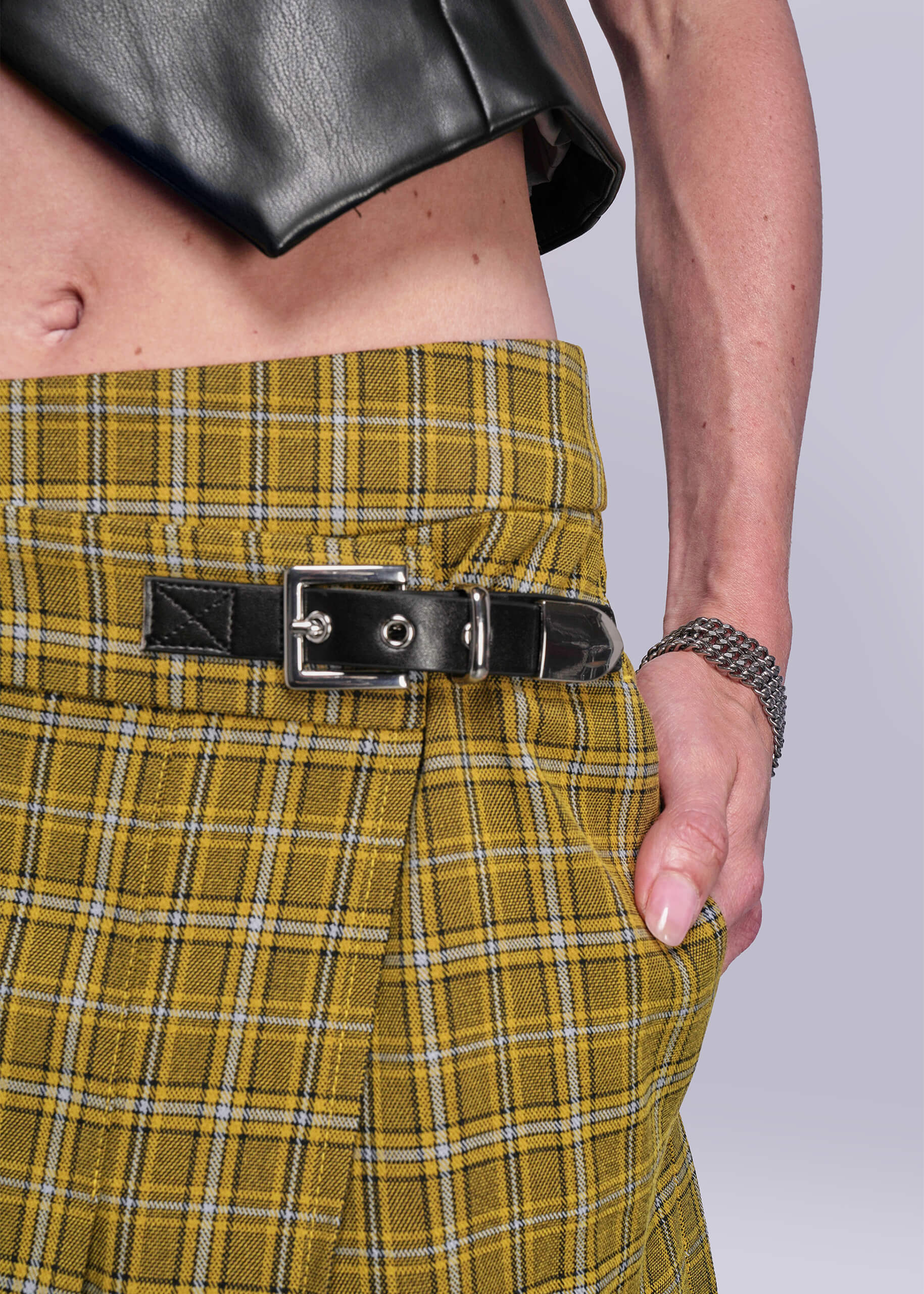 S=Close up view of yellow plaid skirt with a black buckle on a plain background