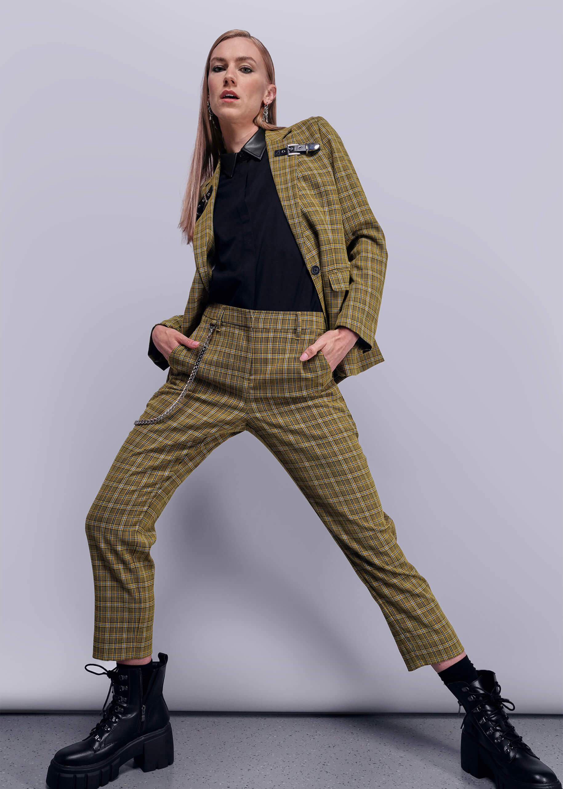 S=Person wearing a yellow plaid suit with black boots on a gray background