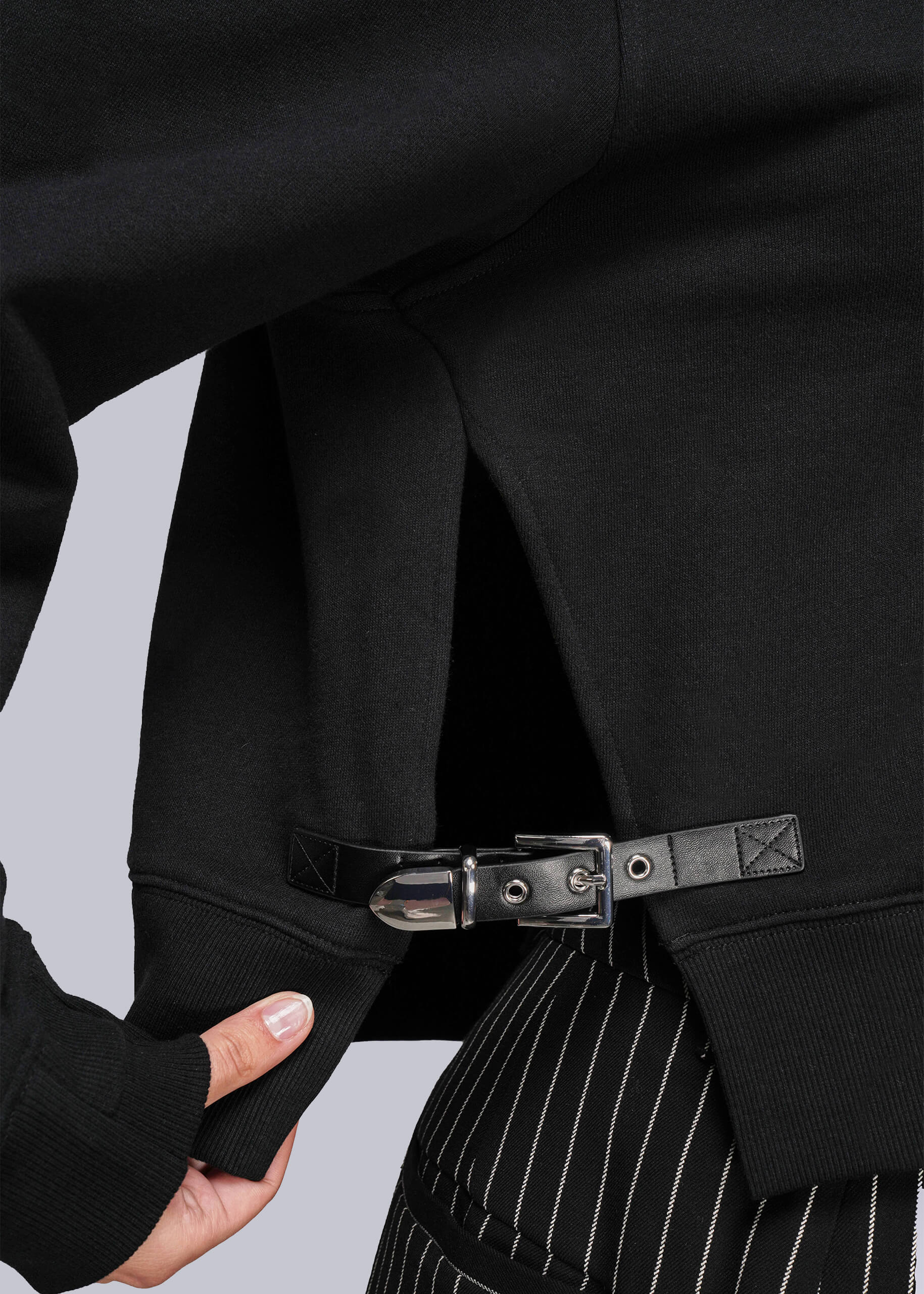 Close-up of a sweatshirt with buckle and pinstripe pants on a light gray background