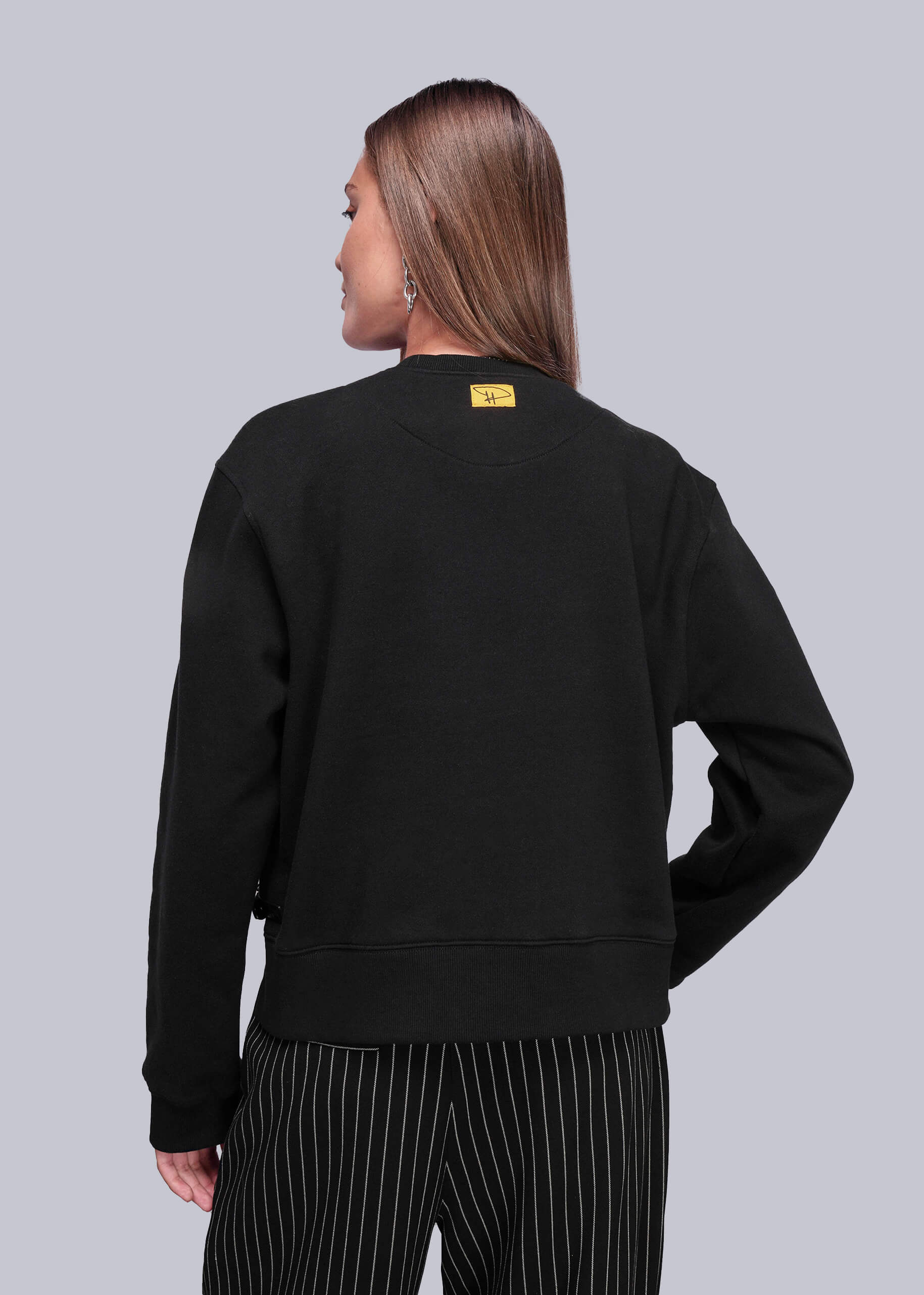 S=Back view of person wearing a black sweatshirt with a yellow label on the back against a light gray background