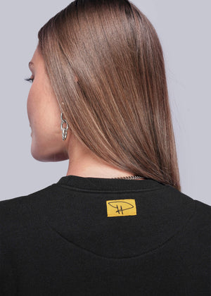 S=Close up of back of person wearing a black sweatshirt with a yellow logo on a plain background