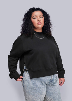 1X=Person wearing a black sweatshirt and light blue jeans against a gray background