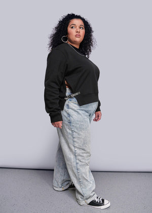 1X=Person wearing a black sweatshirt and light blue jeans against a gray background