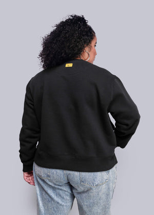 1X=Person wearing a black sweatshirt with a yellow tag on a plain background