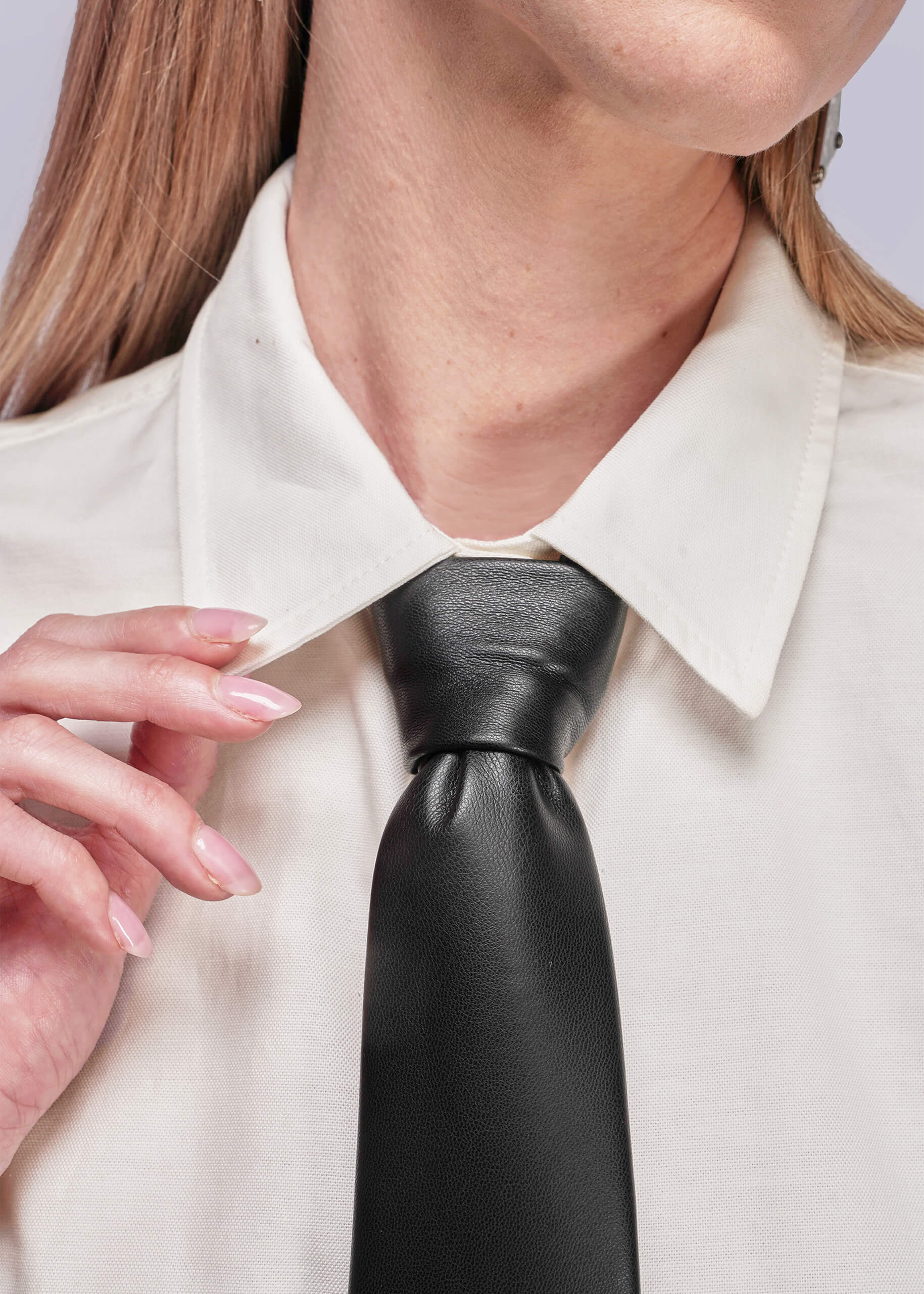 Person wearing a white shirt and black leather tie with a neutral background