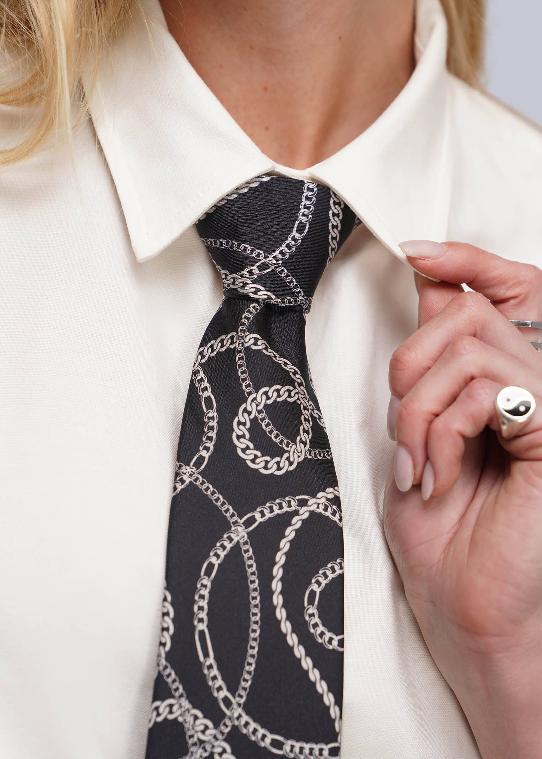 A close-up of a person wearing a black necktie with a silver chain-link pattern, styled with a white collared shirt.
