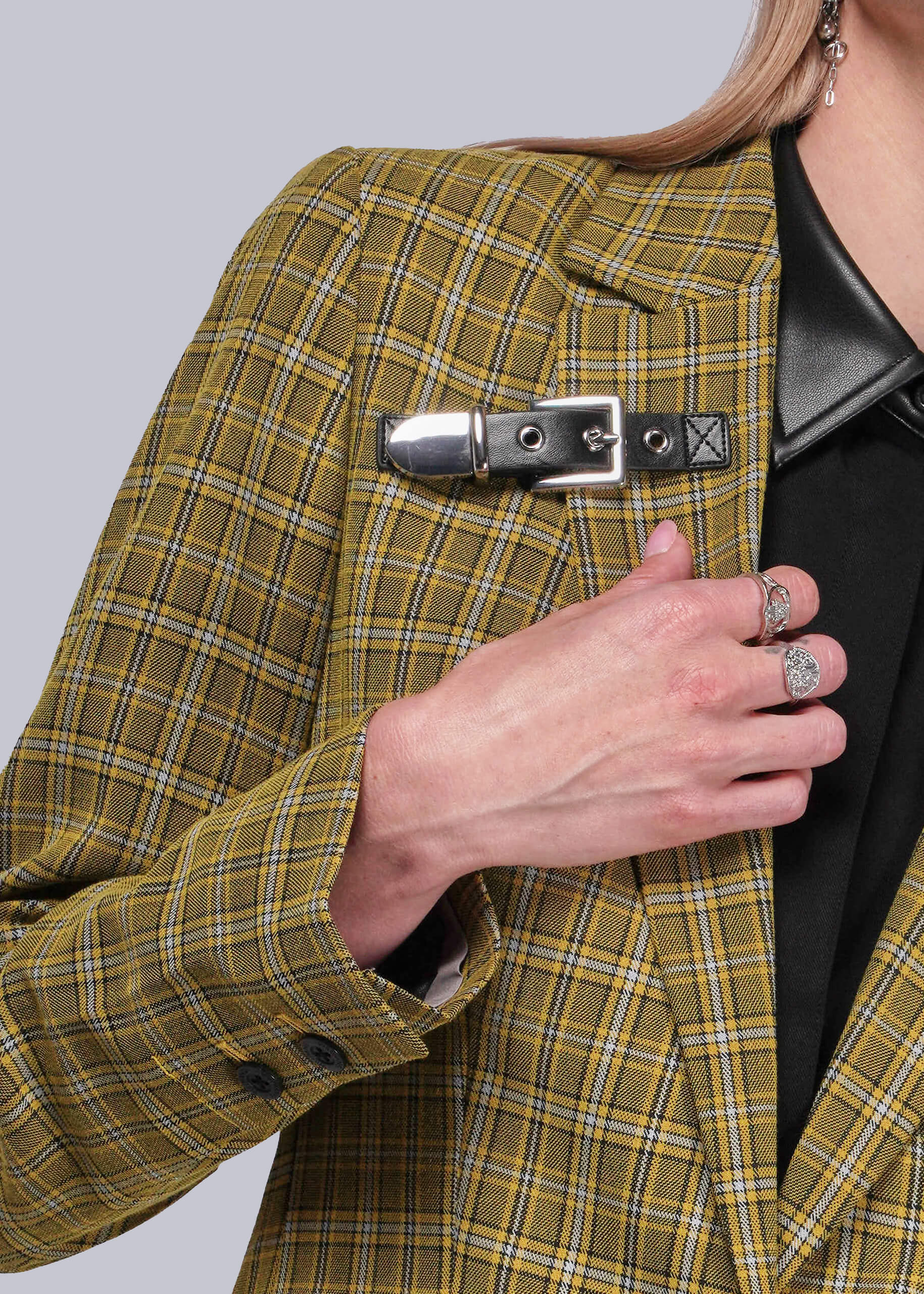 Person wearing a yellow plaid blazer with a black leather buckle detail on a plain background