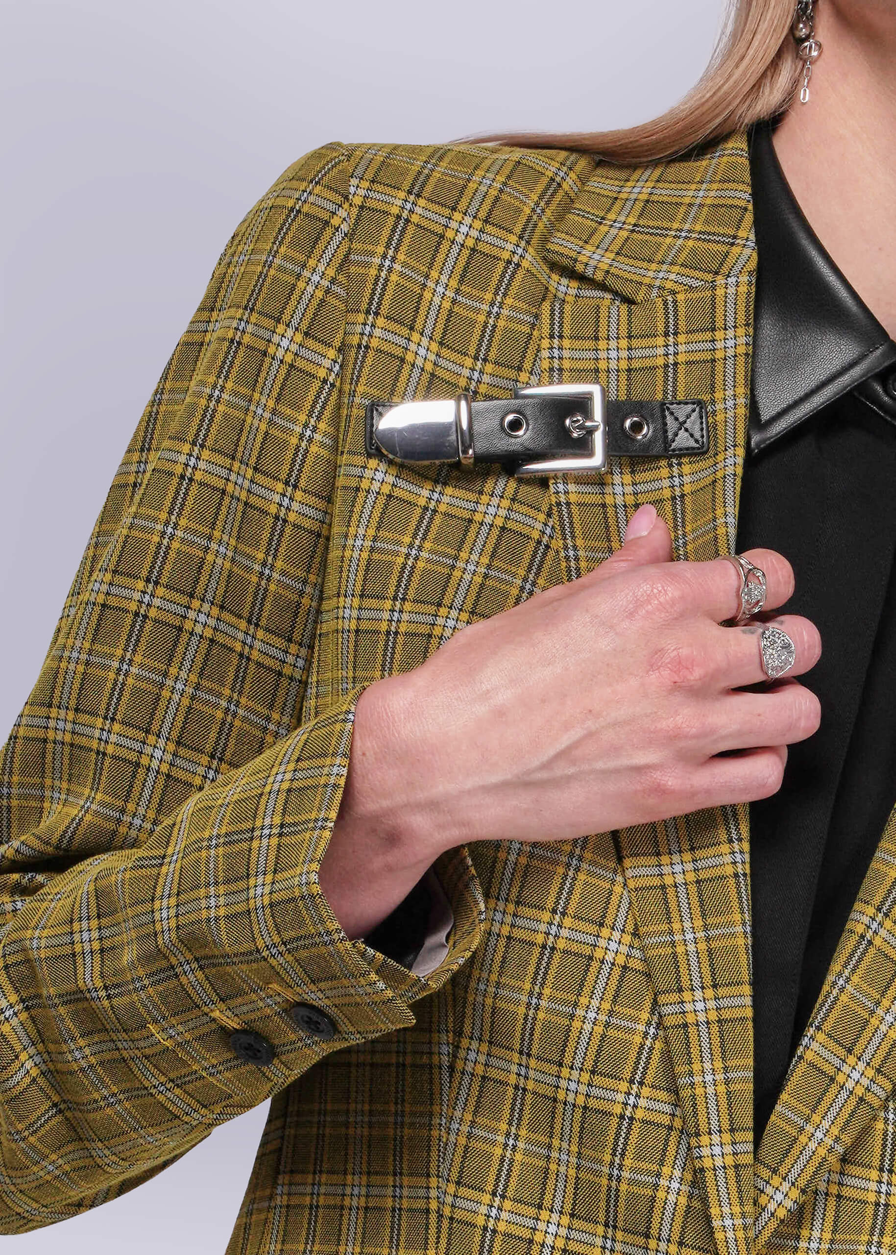 S=Person wearing a yellow plaid blazer with a black leather buckle detail on a plain background