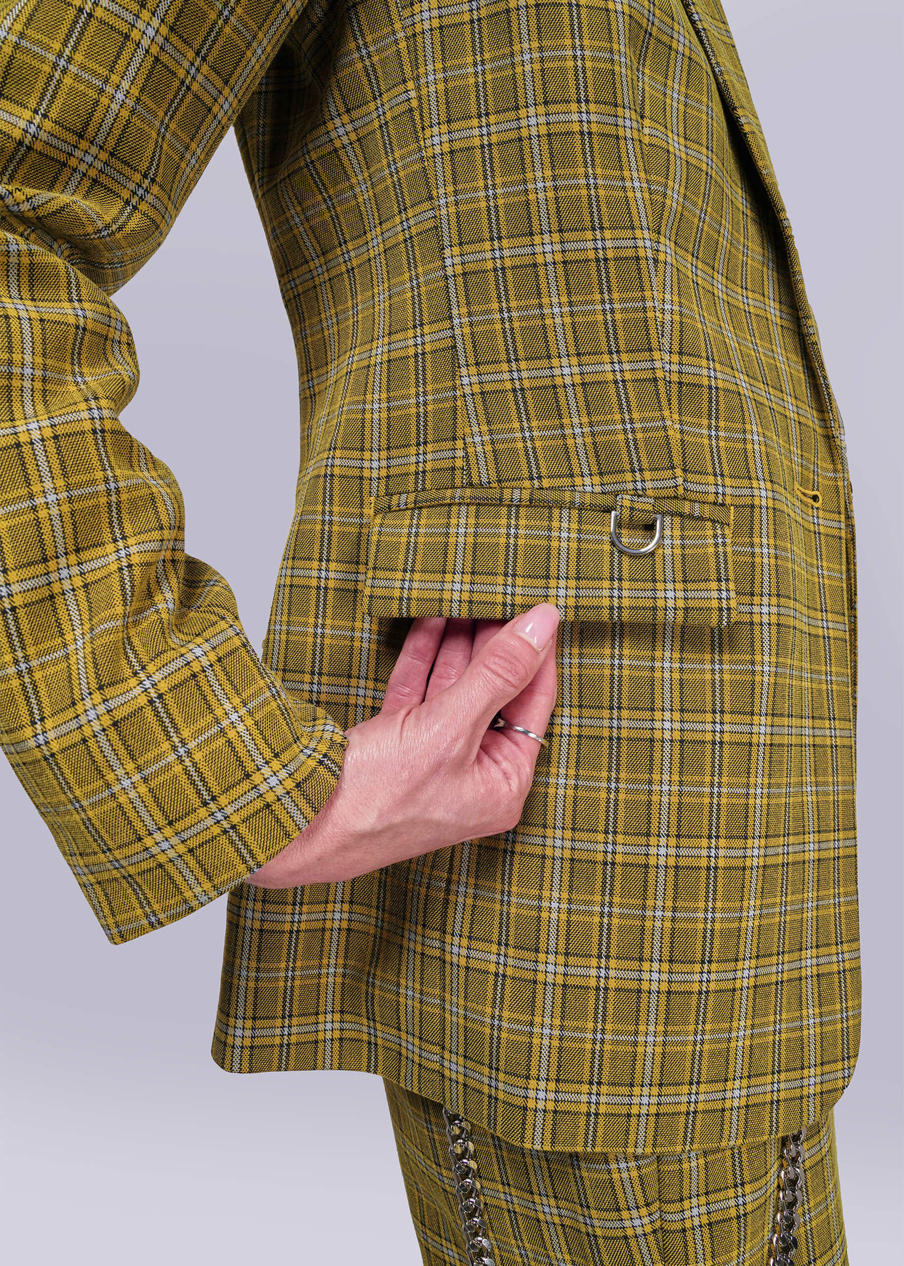 S=Close up of yellow plaid blazer with a hand touching the pocket flap on a light gray background