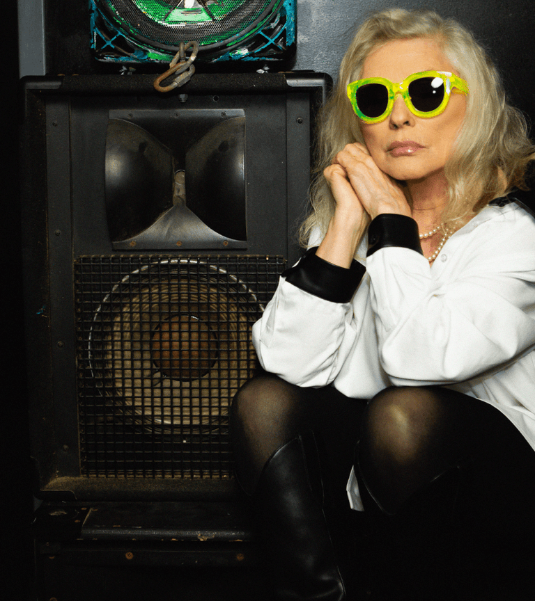 Person wearing bright yellow sunglasses sitting in front of a large speaker.