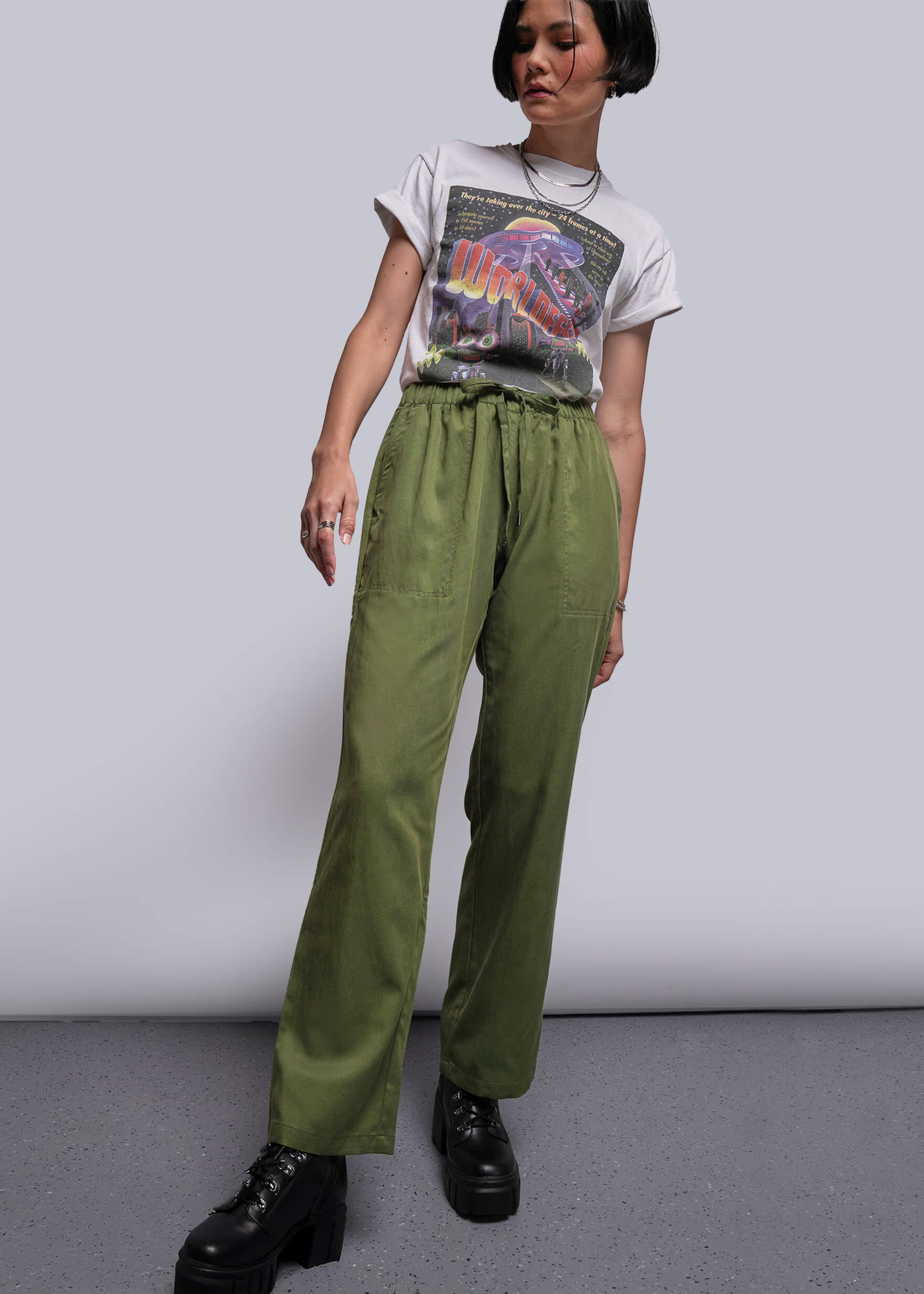 Person wearing a graphic t-shirt and green pants against a plain background