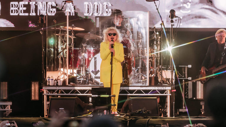 Person on stage with text projected on screens, surrounded by equipment and audience.