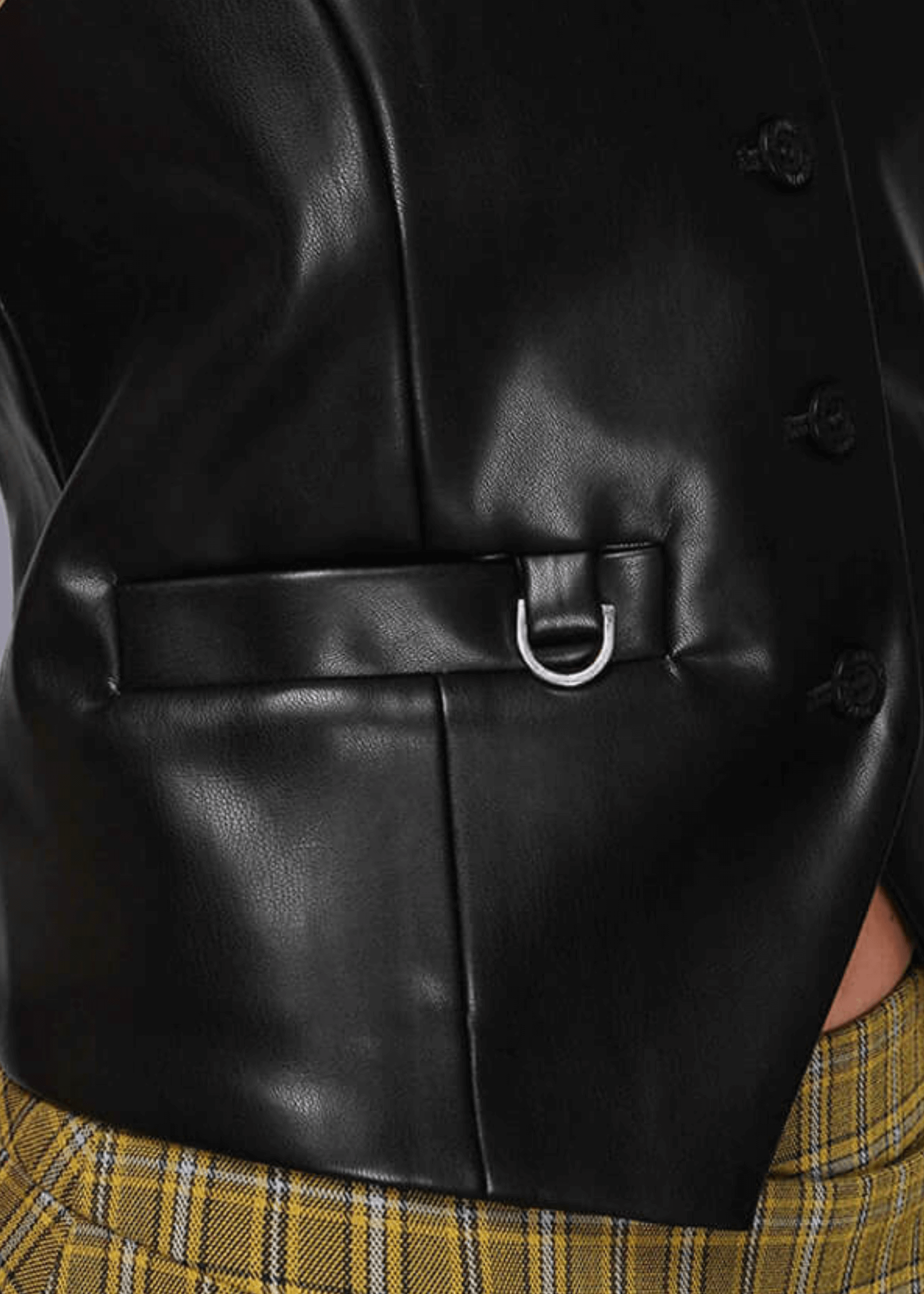 Close-up of a black vegan leather vest with a belt and plaid pants.
