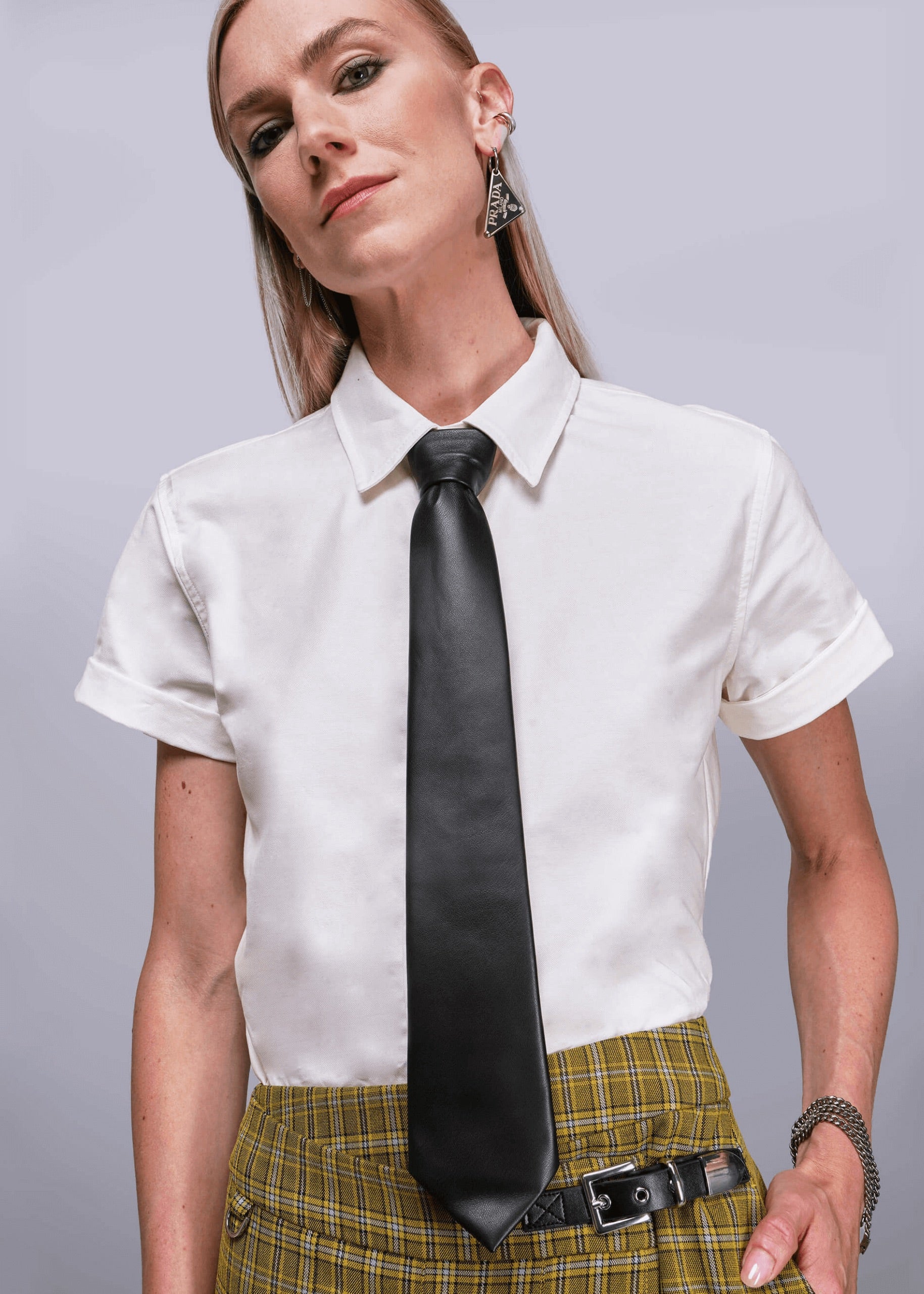Person wearing a white shirt with a long black tie and plaid skirt on a gray background