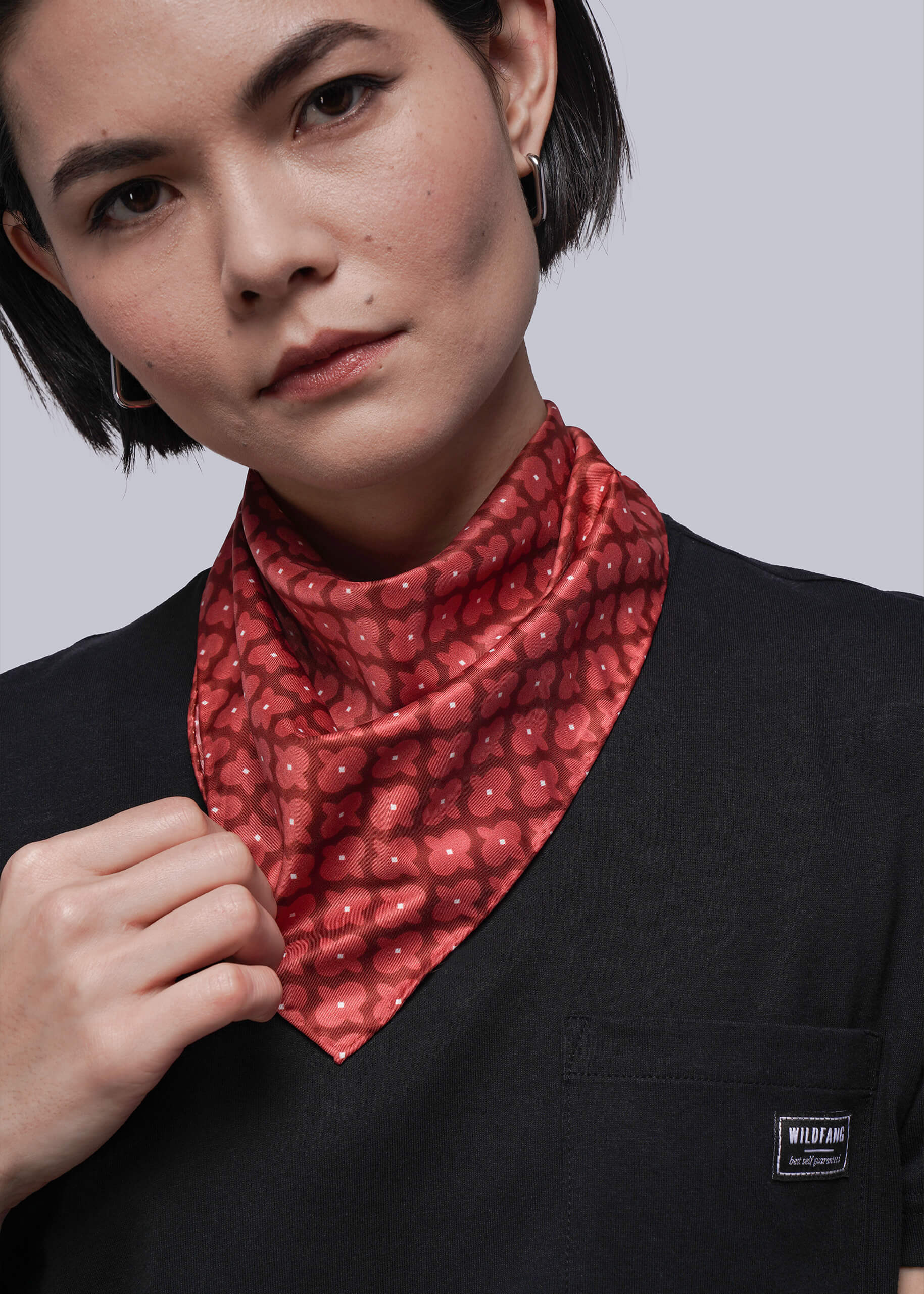 Person wearing a red patterned scarf with a black shirt on a gray background