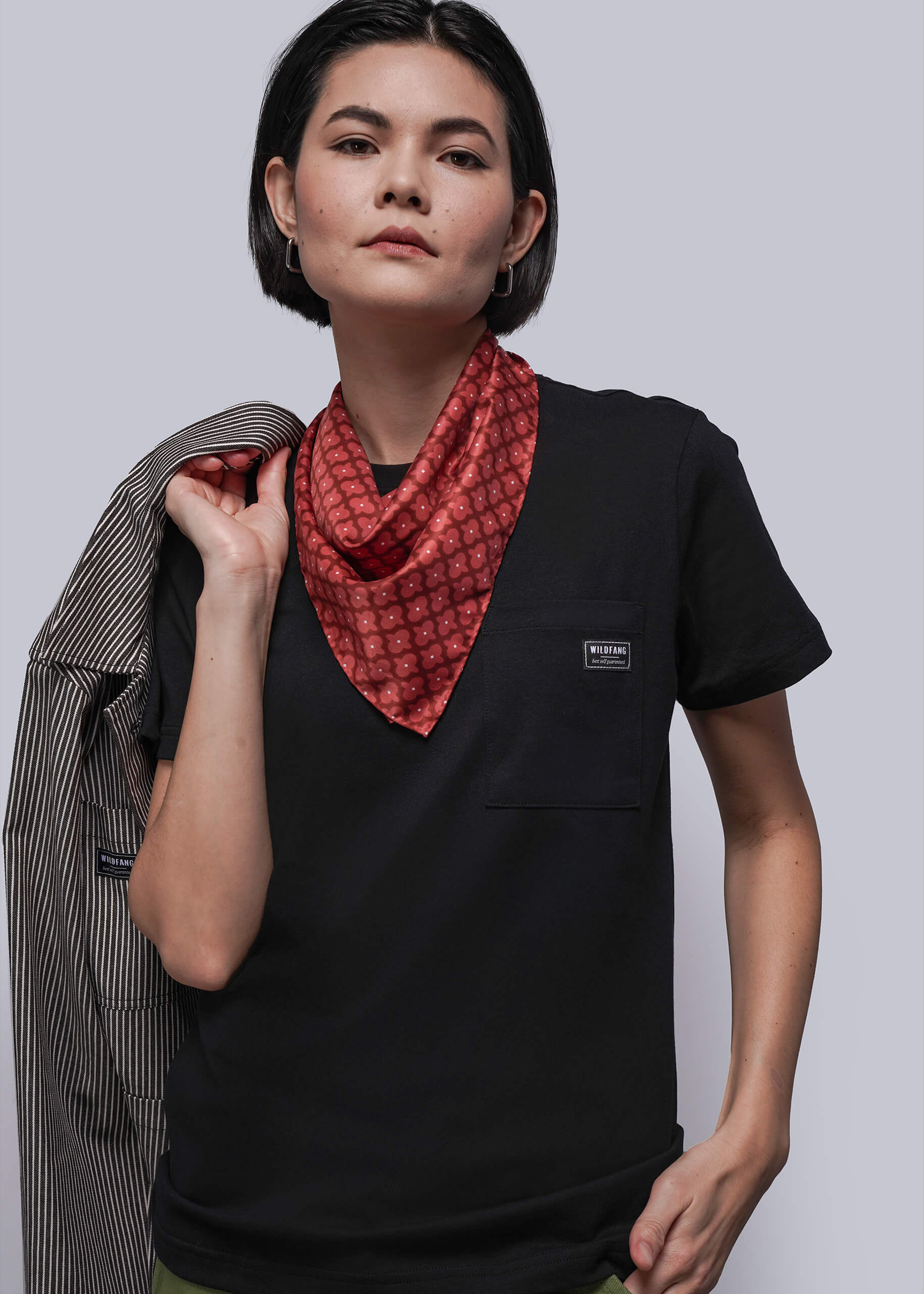 Person wearing a black t-shirt with a red patterned scarf, holding a striped jacket.