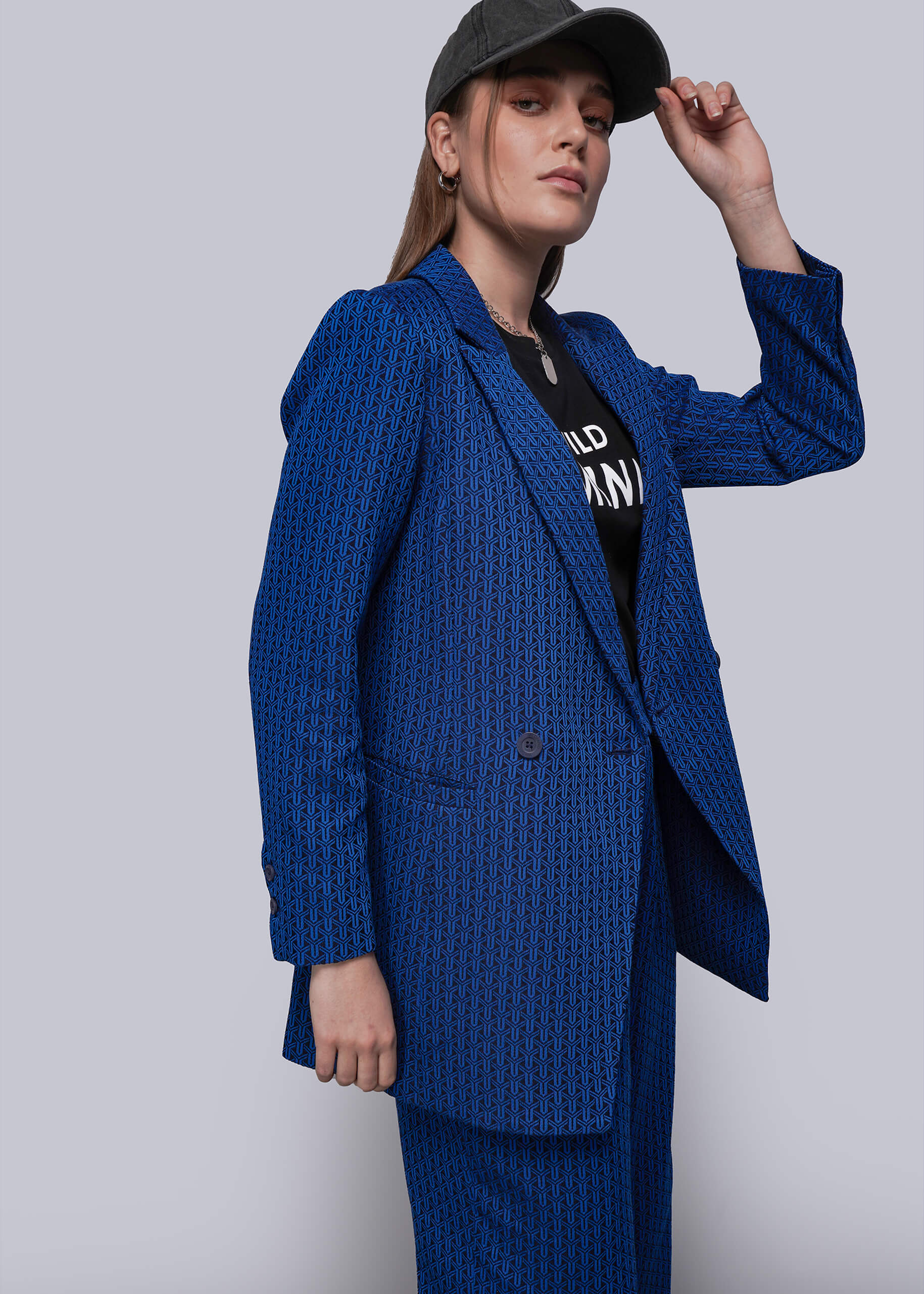 S=Person wearing a blue textured suit and black cap against a white background