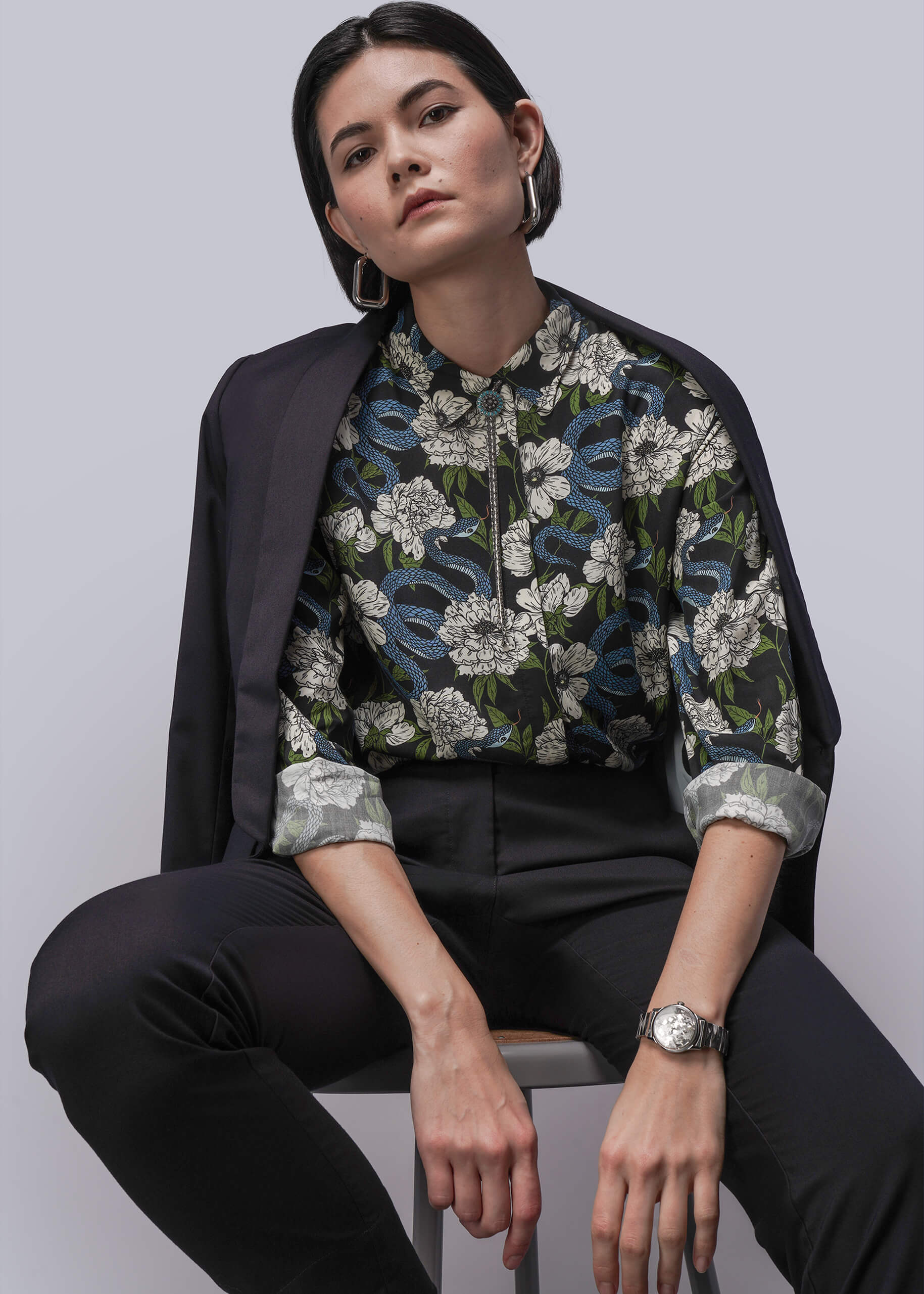 Person wearing a floral blouse with a black jacket and pants on a plain background
