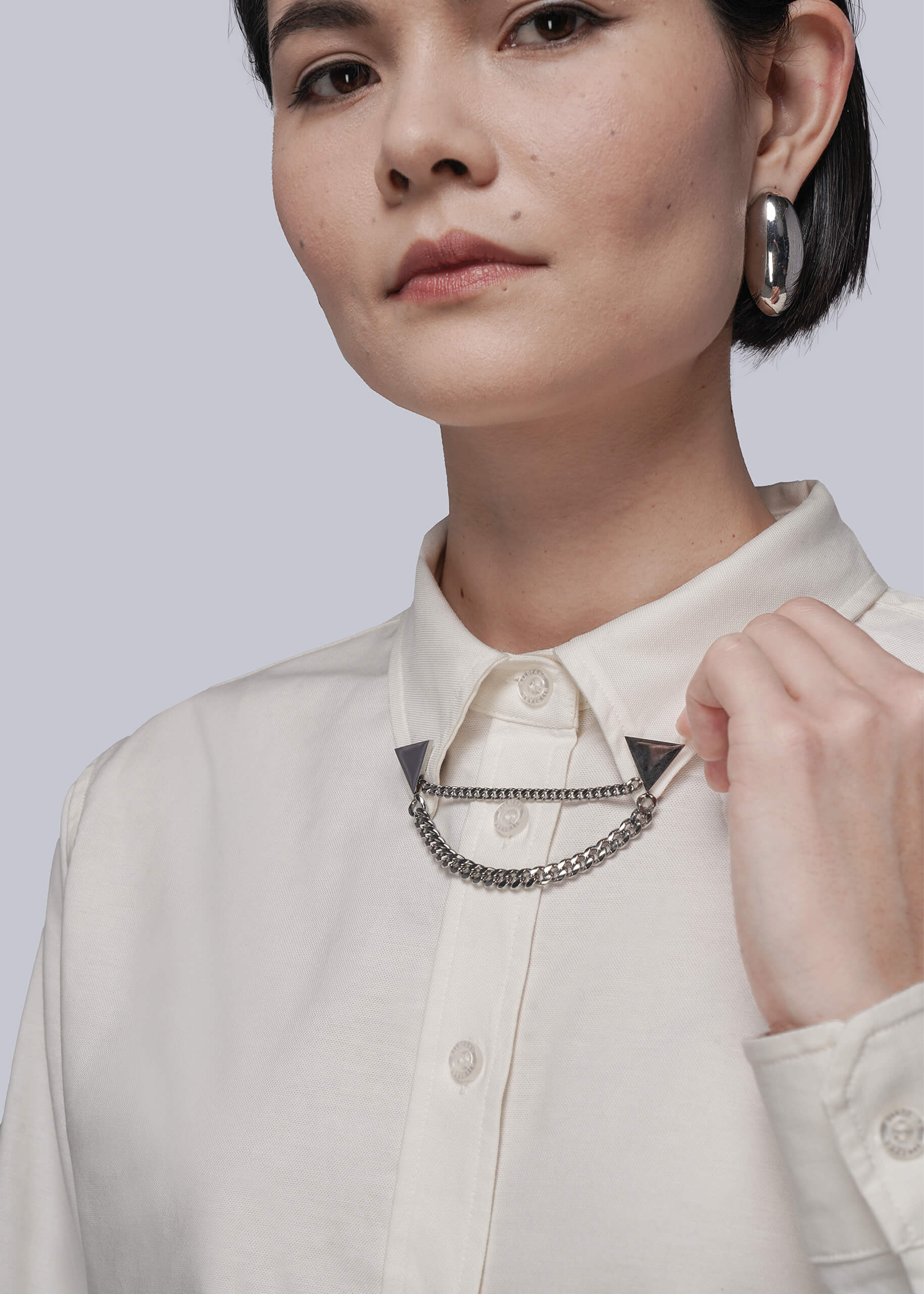 Person wearing a white shirt with a chain collar clips, against a plain background
