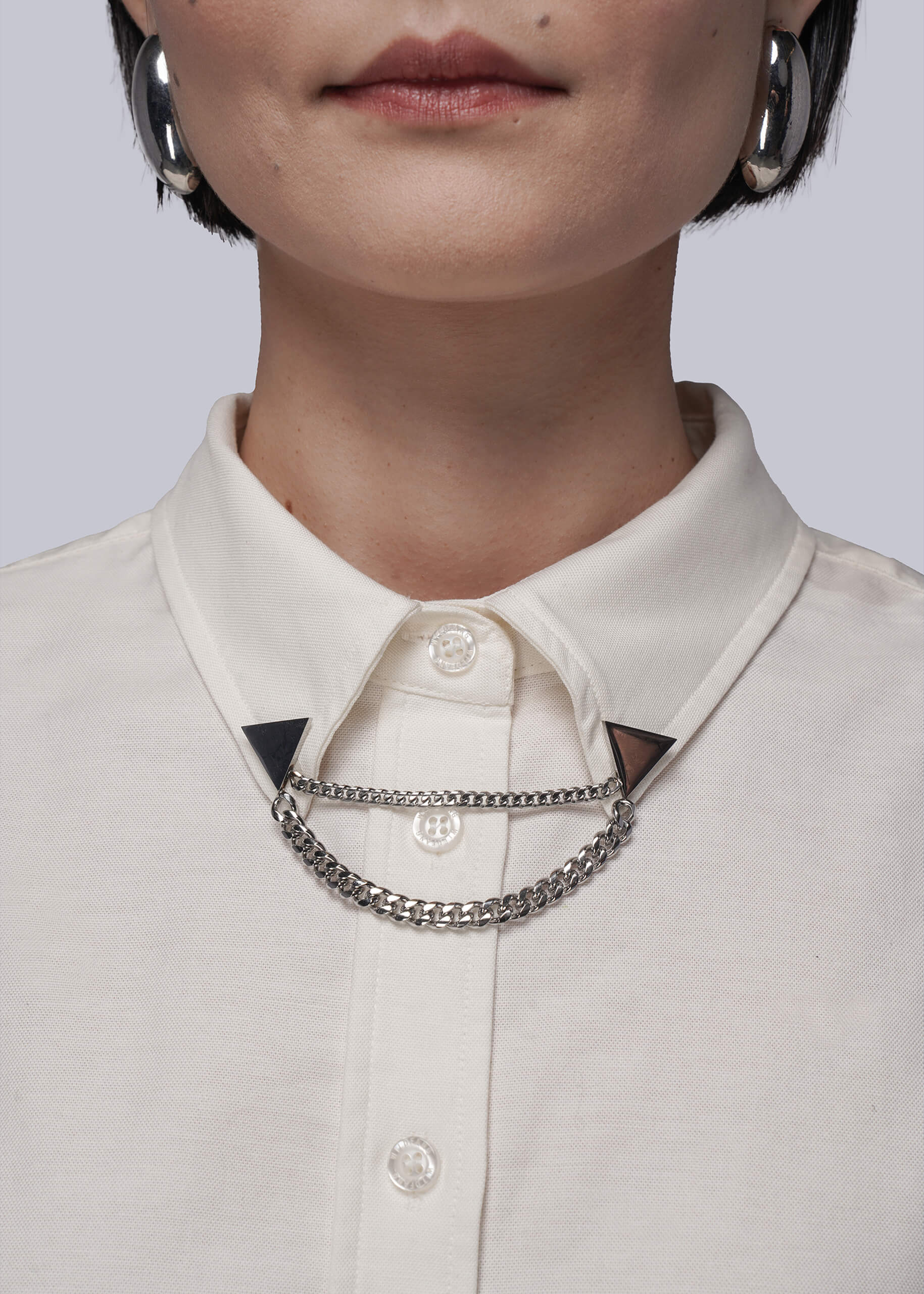 Close-up of a person wearing a light-colored shirt with a chain collar clips against a neutral background