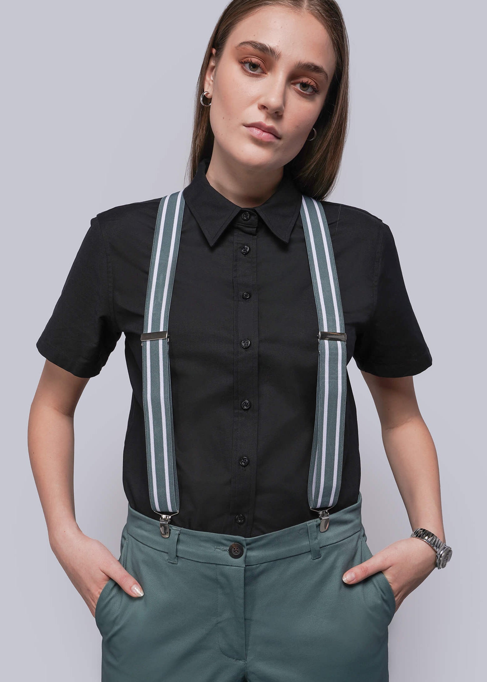 Person wearing a black shirt with teal and white stripe suspenders and teal pants on a plain background