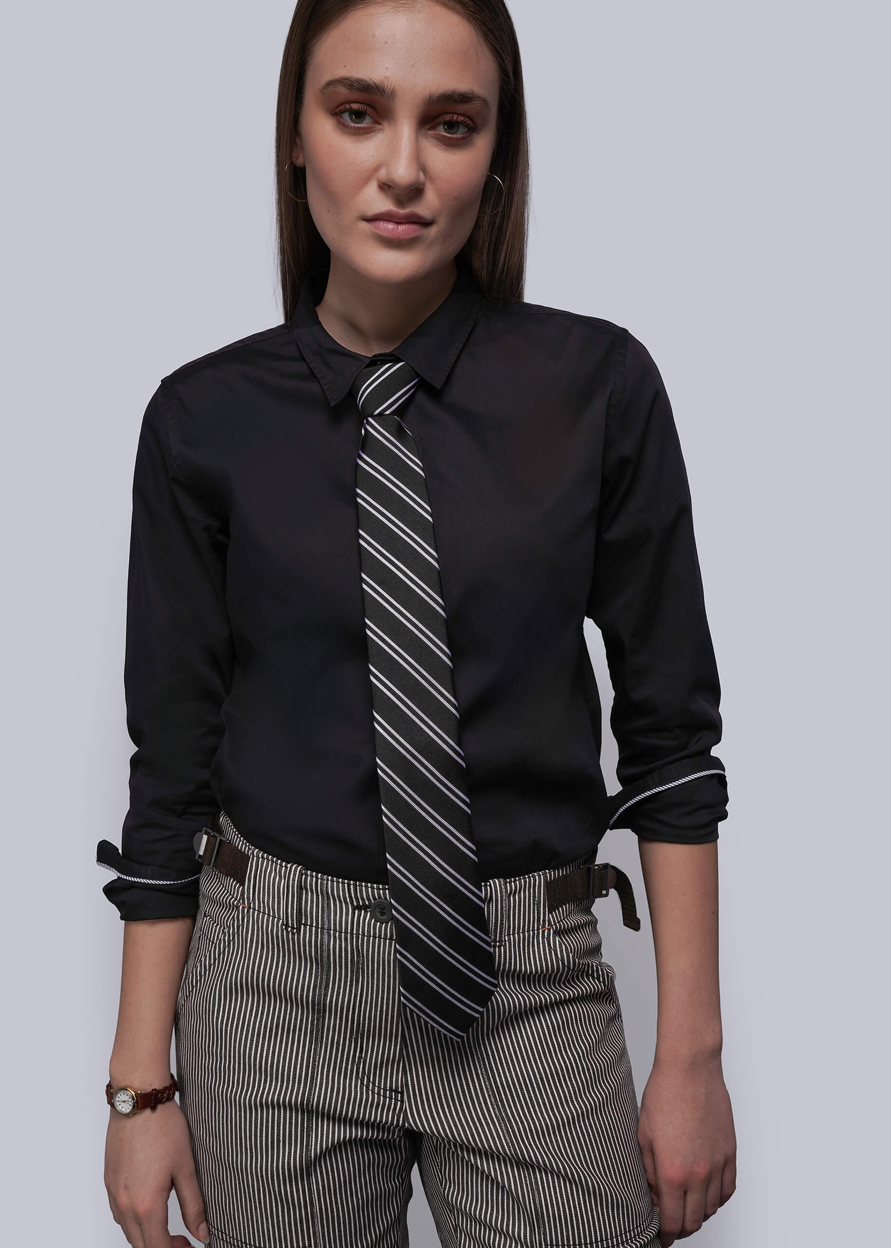 Person wearing a black dress shirt with a striped tie and gray pants on a white background