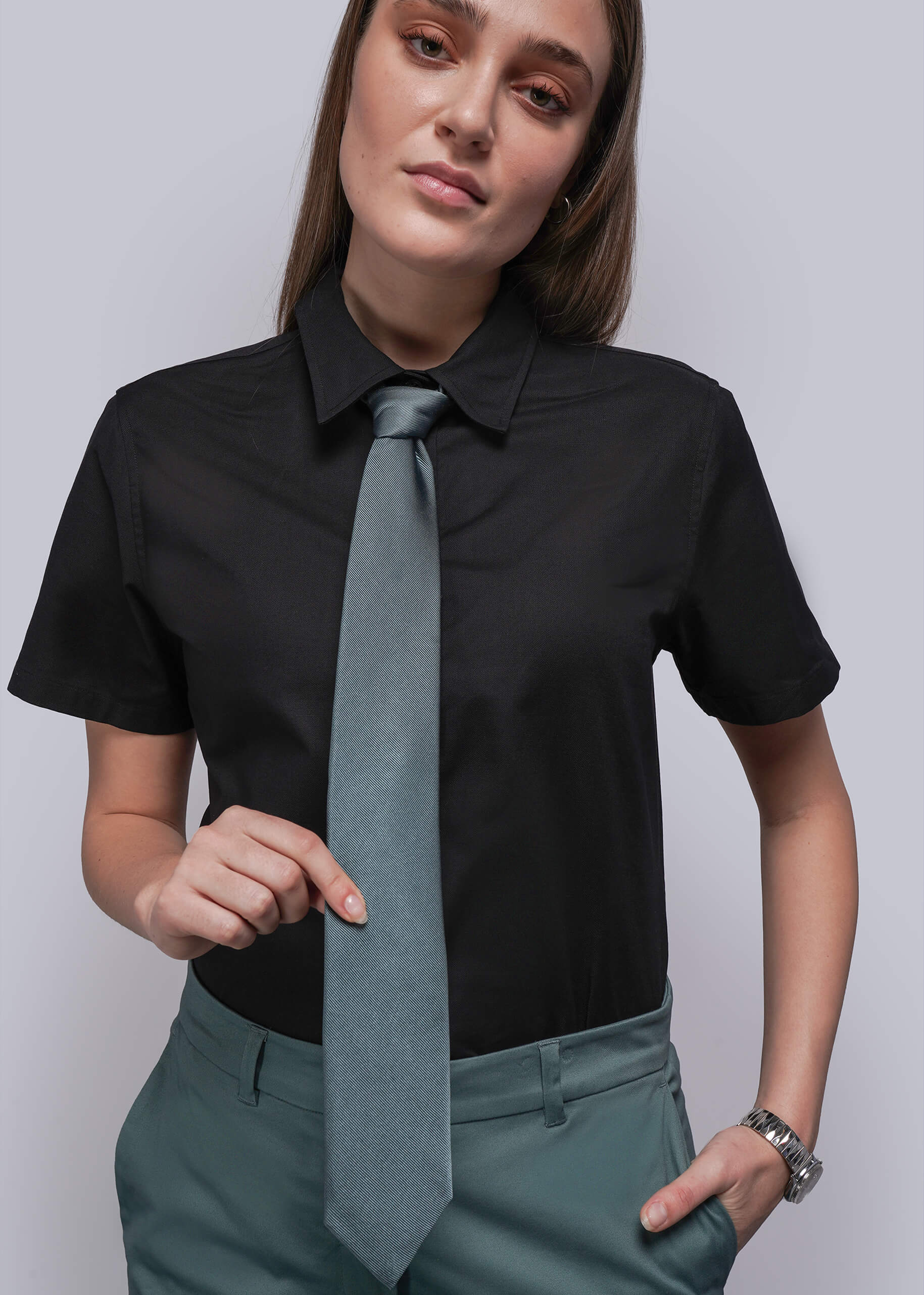 Woman wearing a black shirt with a long light blue tie against a plain background