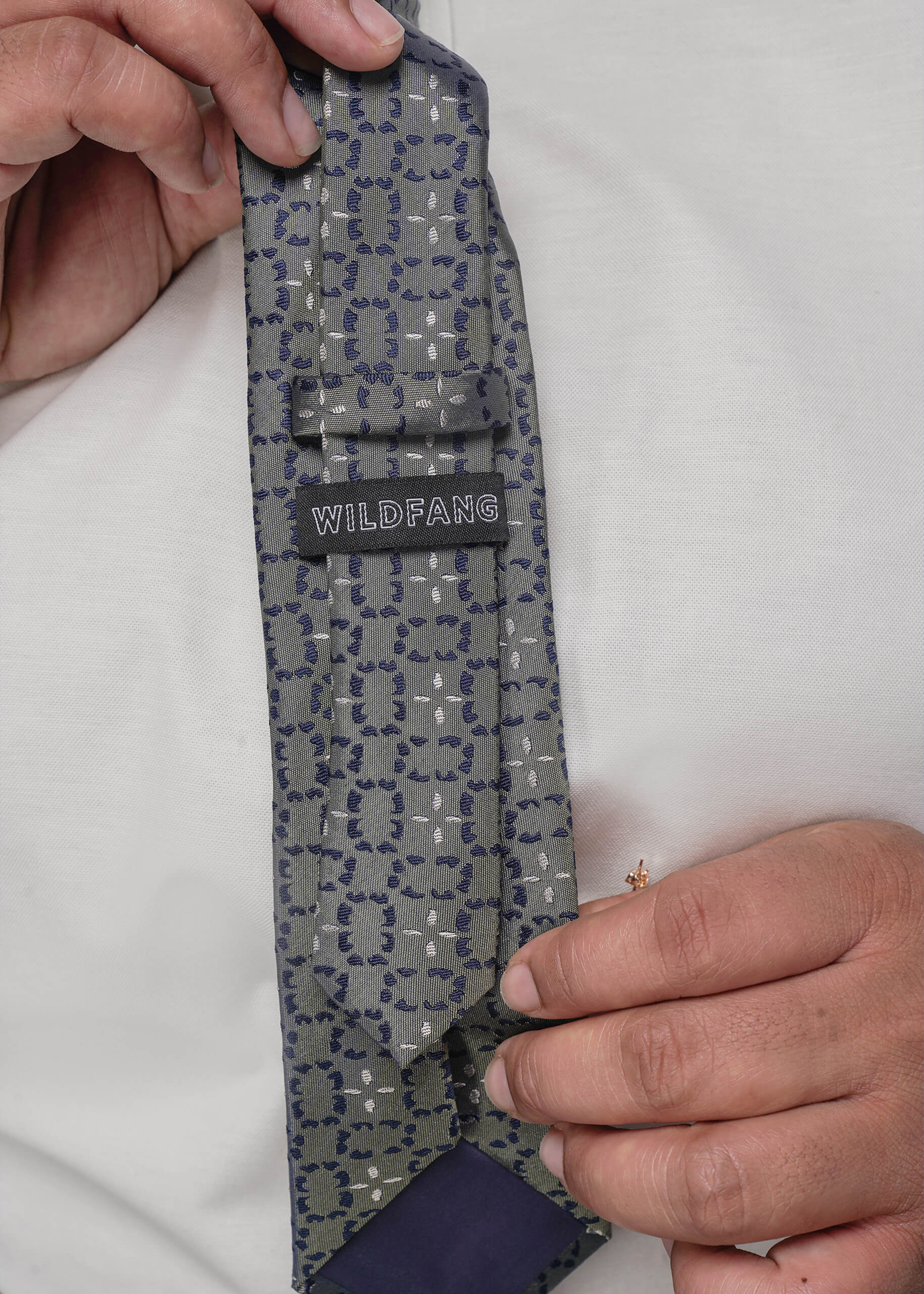 Gray patterned tie with 'WILDFANG' label held by a person against a white background