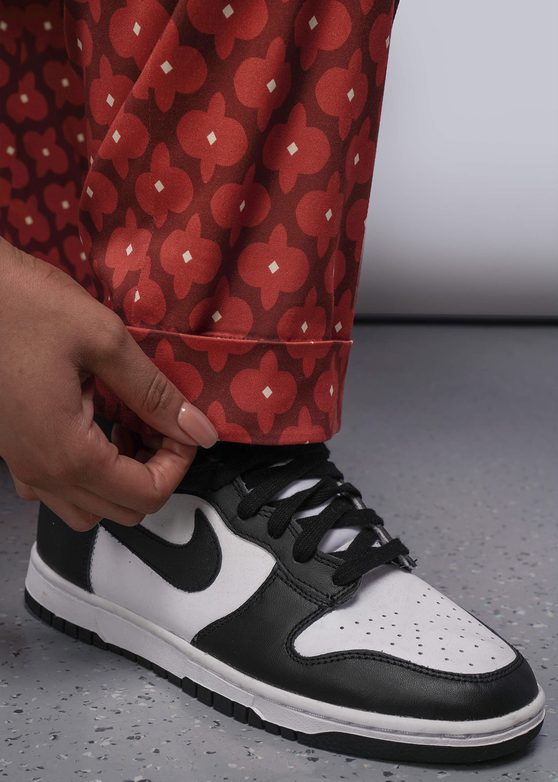 1X=Person wearing black and white sneakers with red patterned pants on a gray floor.